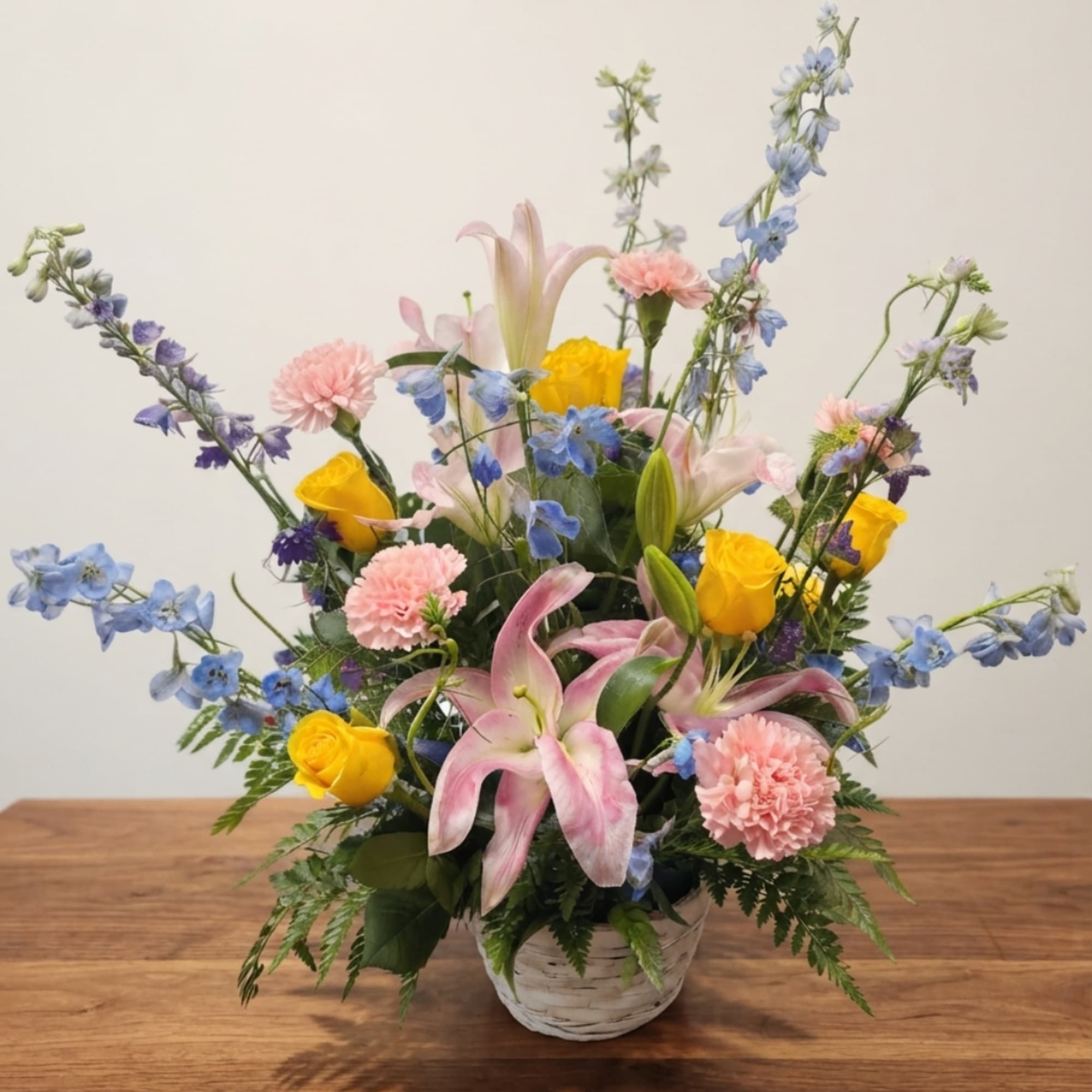 Mixed bouquet in a white basket with pink lilies, yellow roses, and blue flowers, photo 2 of 2