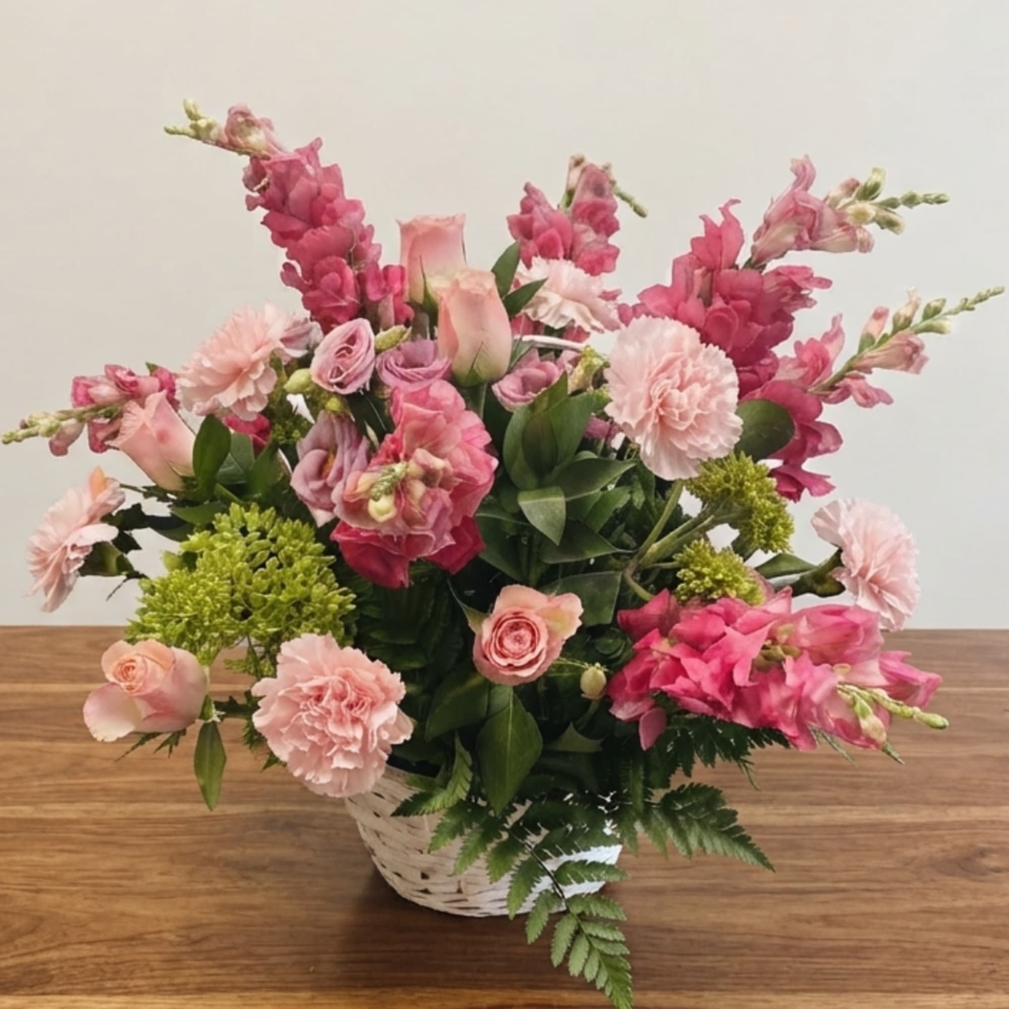 Pink floral arrangement in a white basket with mixed blooms
