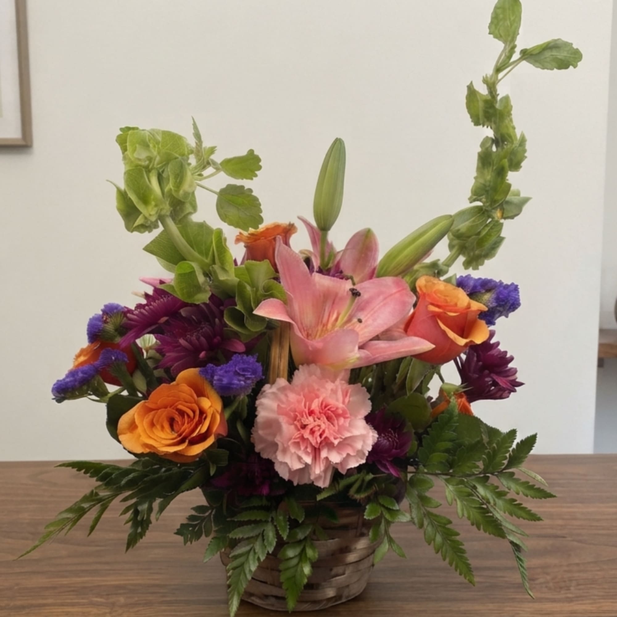 Mixed flower arrangement in a woven basket with pink lilies and orange roses