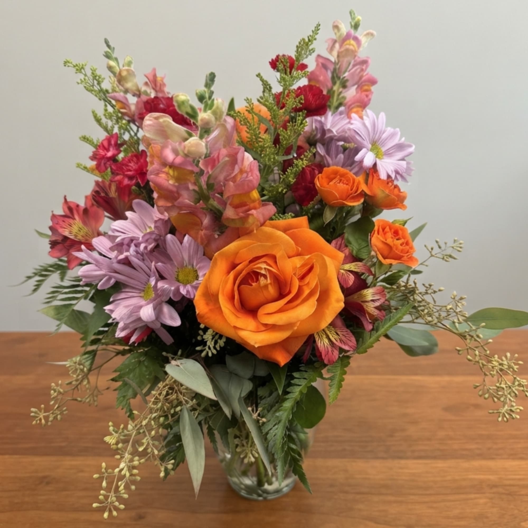 Orange roses and lavender daisies in a clear glass vase