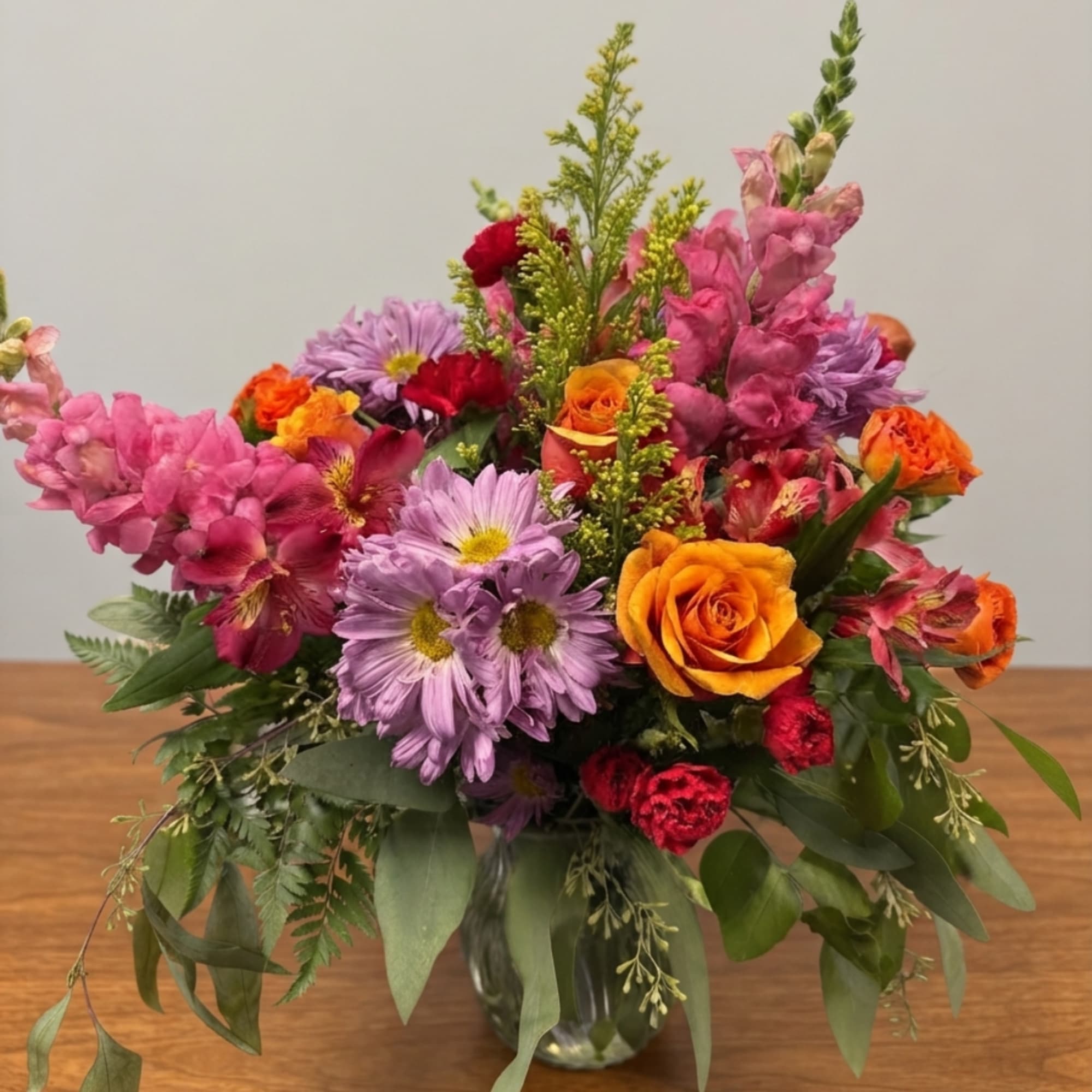 Colorful mixed bouquet in a clear glass vase with roses and daisy-like blooms