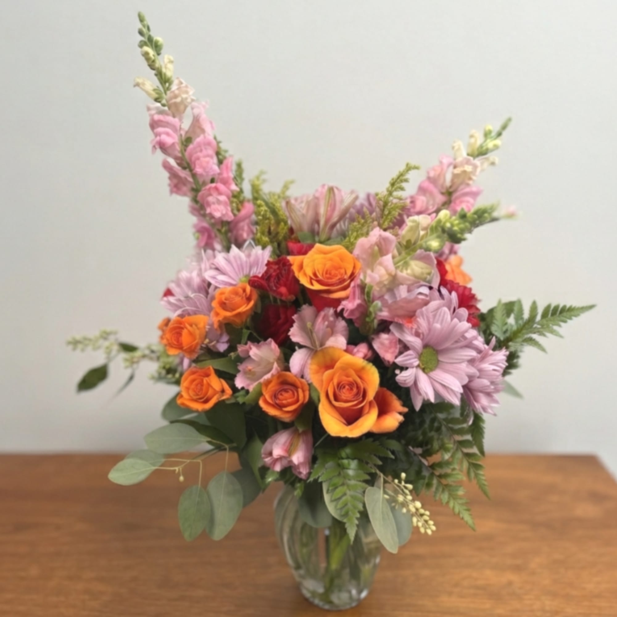Mixed bouquet of orange roses and pink flowers in a glass vase