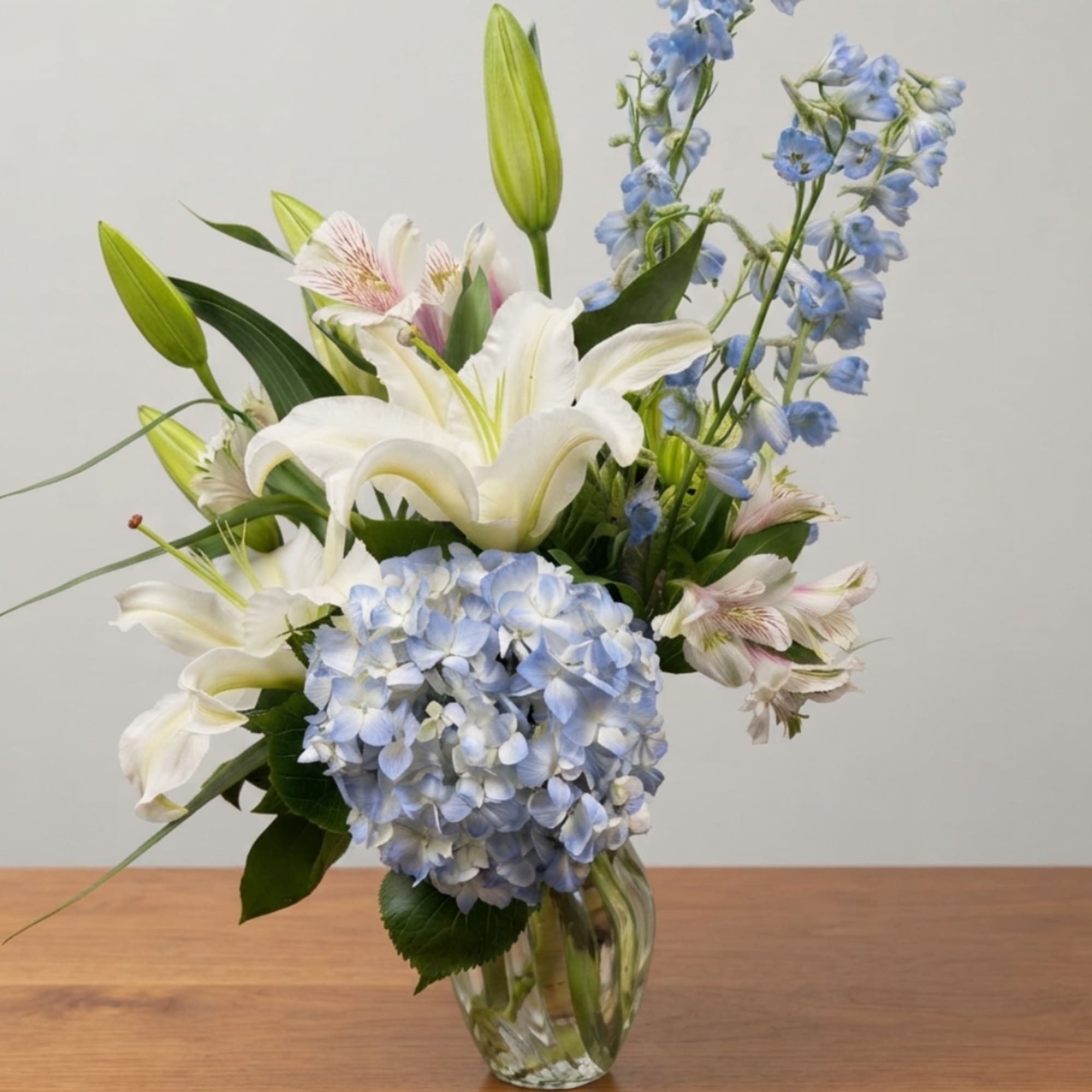 White lilies and blue hydrangeas in a clear glass vase