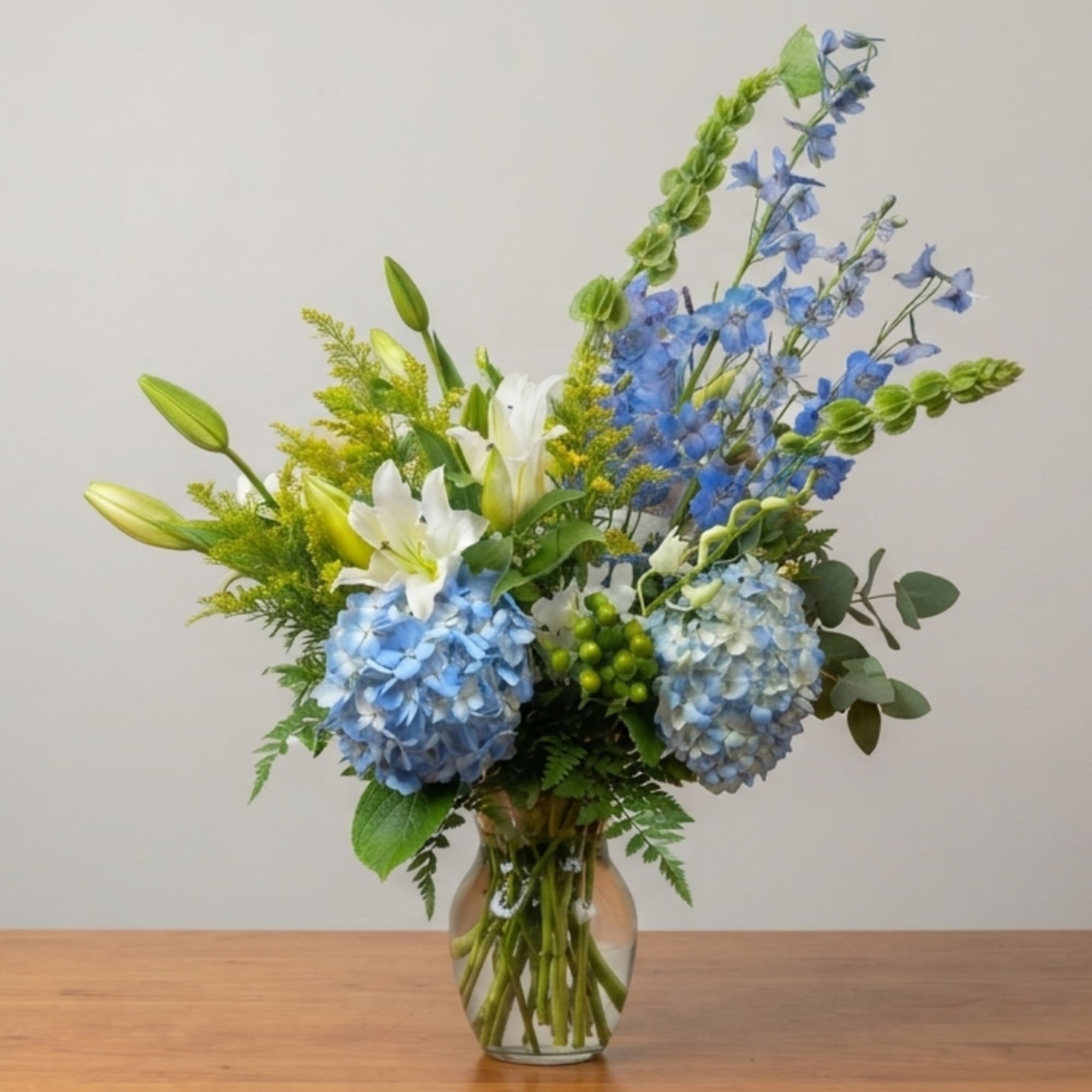Blue hydrangeas and white lilies in a clear glass vase, photo 2 of 3