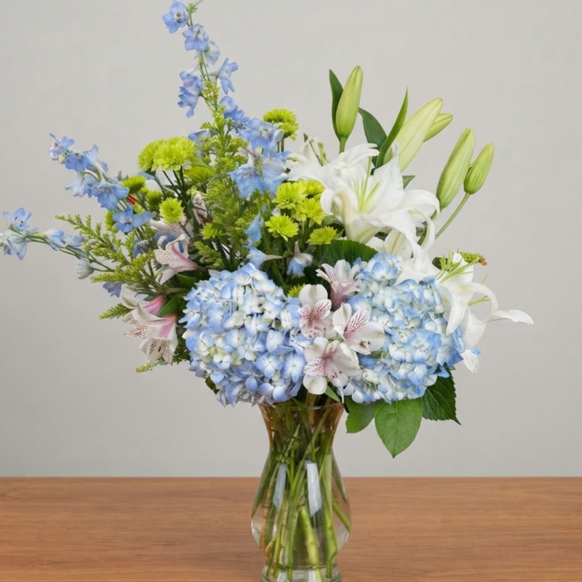Blue hydrangeas and white lilies in a clear glass vase, photo 3 of 3