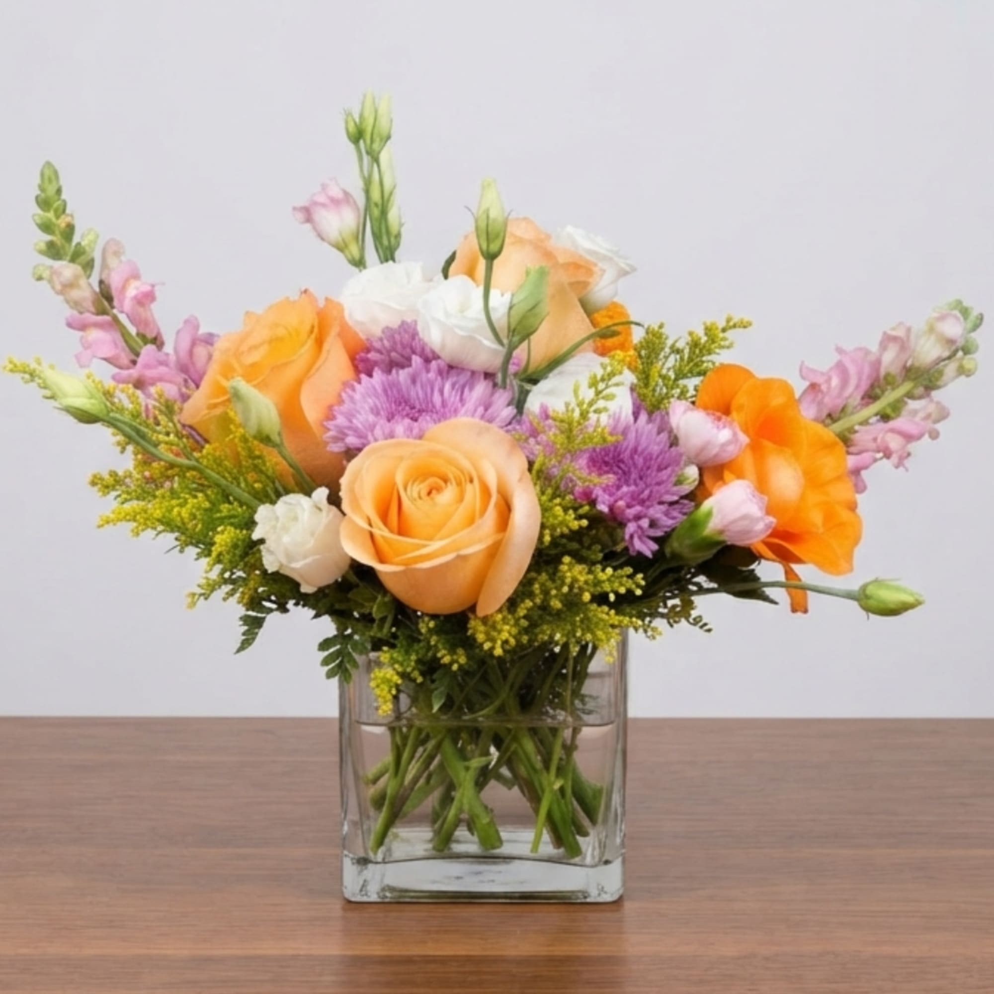 Orange and white roses with purple flowers in a clear square vase