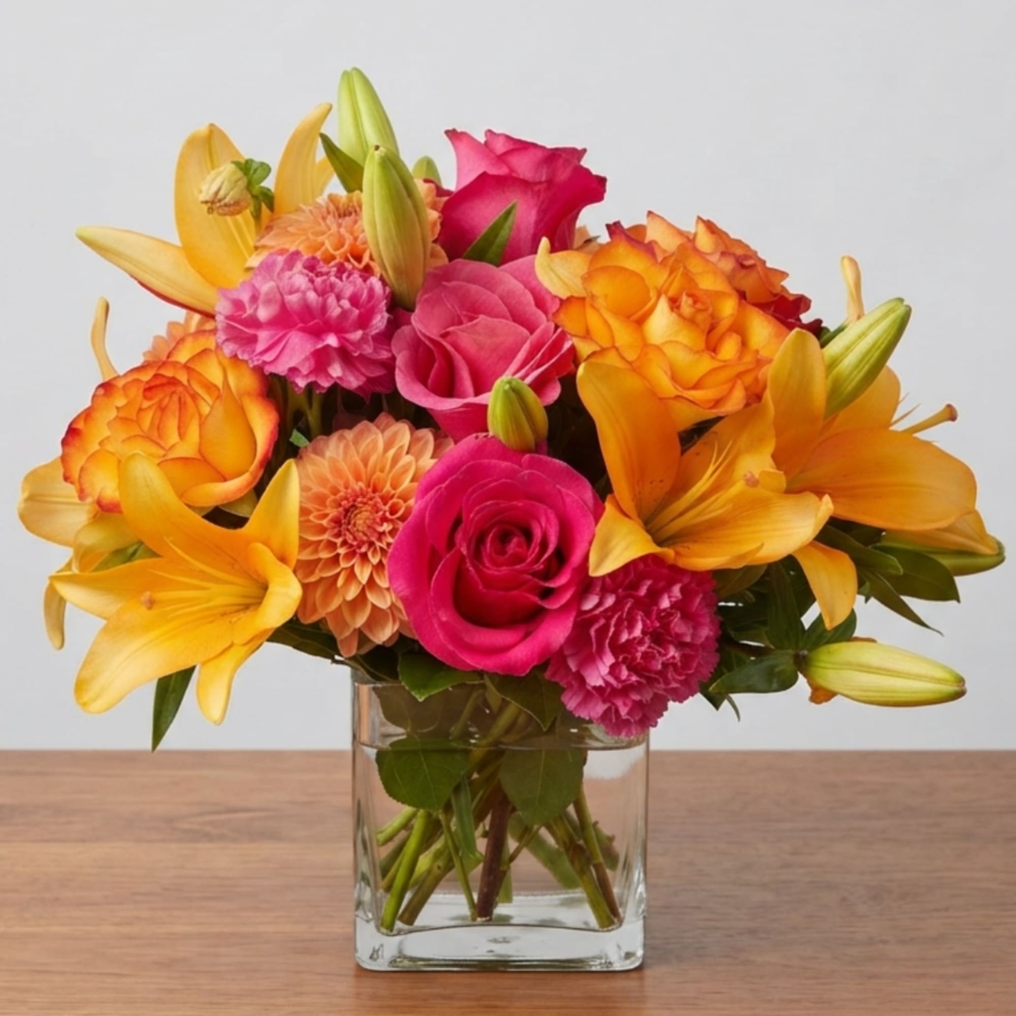 Bright mixed bouquet of roses, lilies, and carnations in a clear glass vase