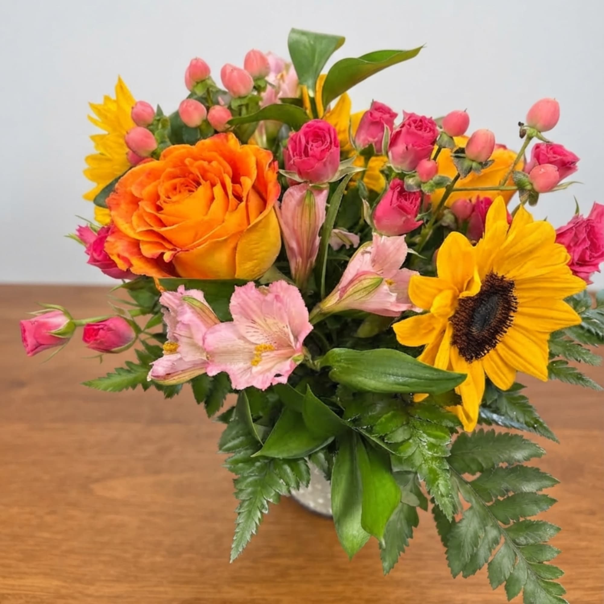 Mixed bouquet with orange rose, yellow sunflowers, and pink blooms in a vase