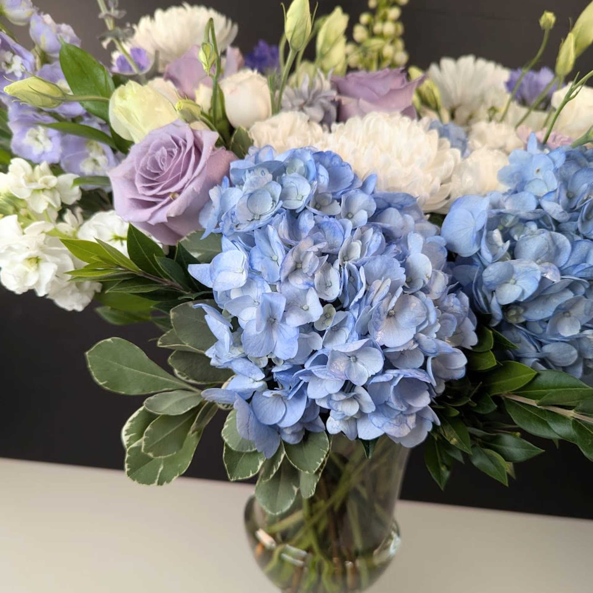 Blue hydrangeas and lavender roses in a clear glass vase