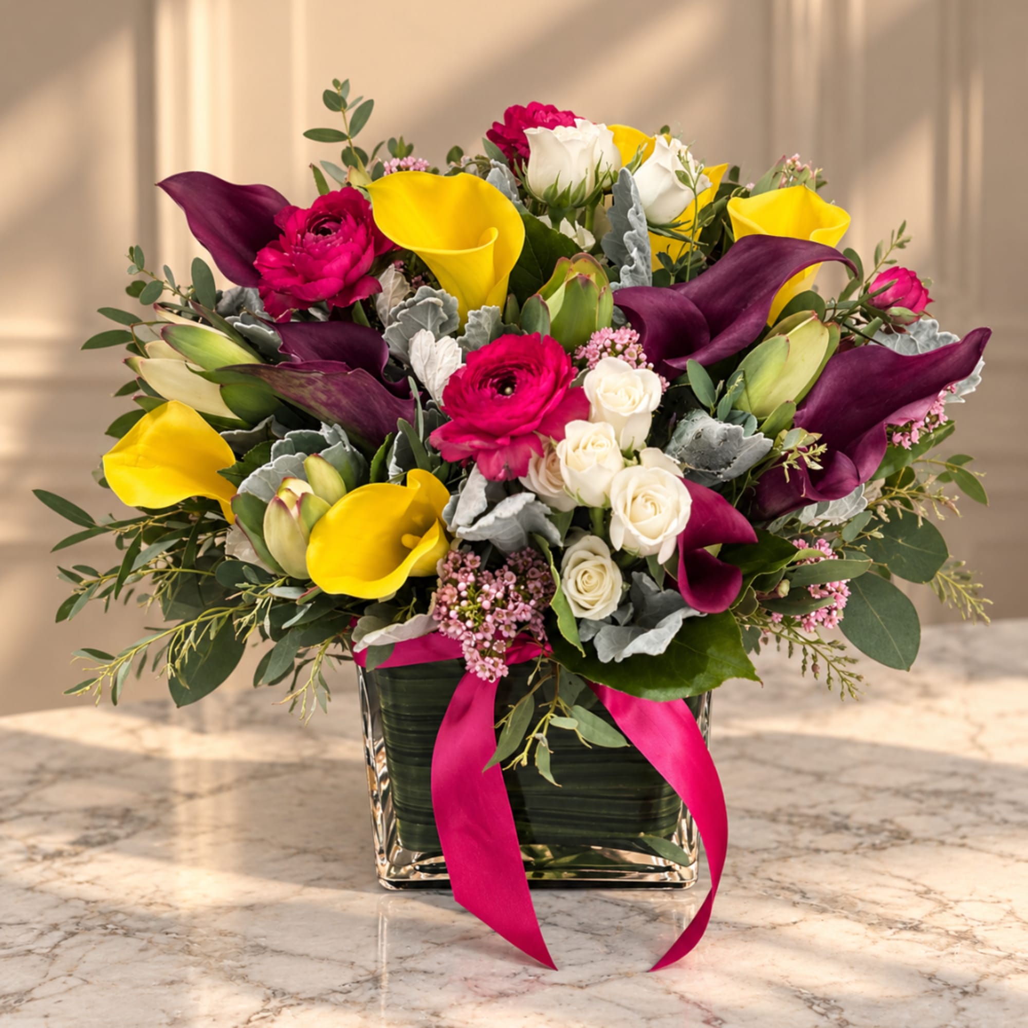 Colorful bouquet of calla lilies, roses, and pink flowers in a square glass vase
