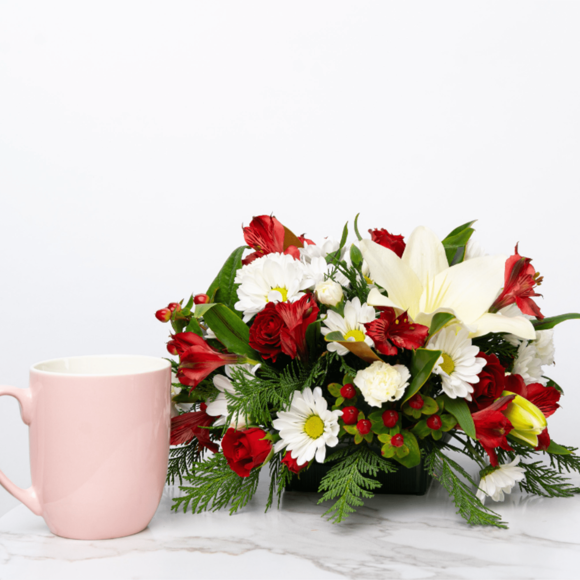 Red and white flower arrangement beside a pink mug
