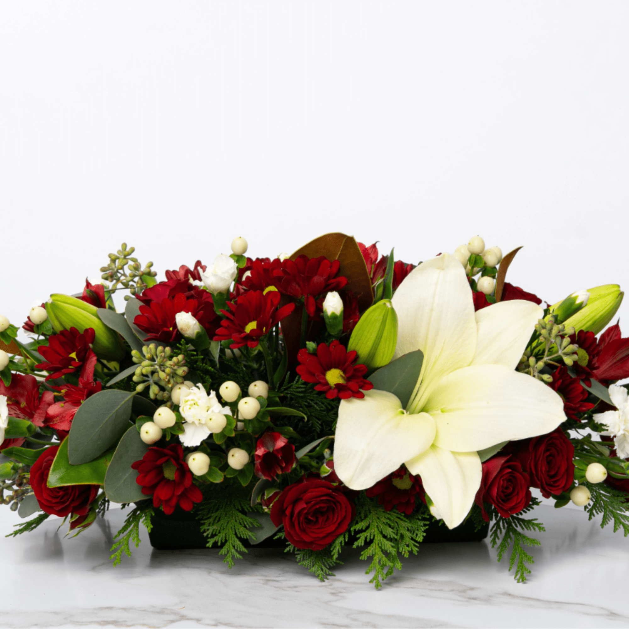 Red and white floral centerpiece with lilies and roses in a low container