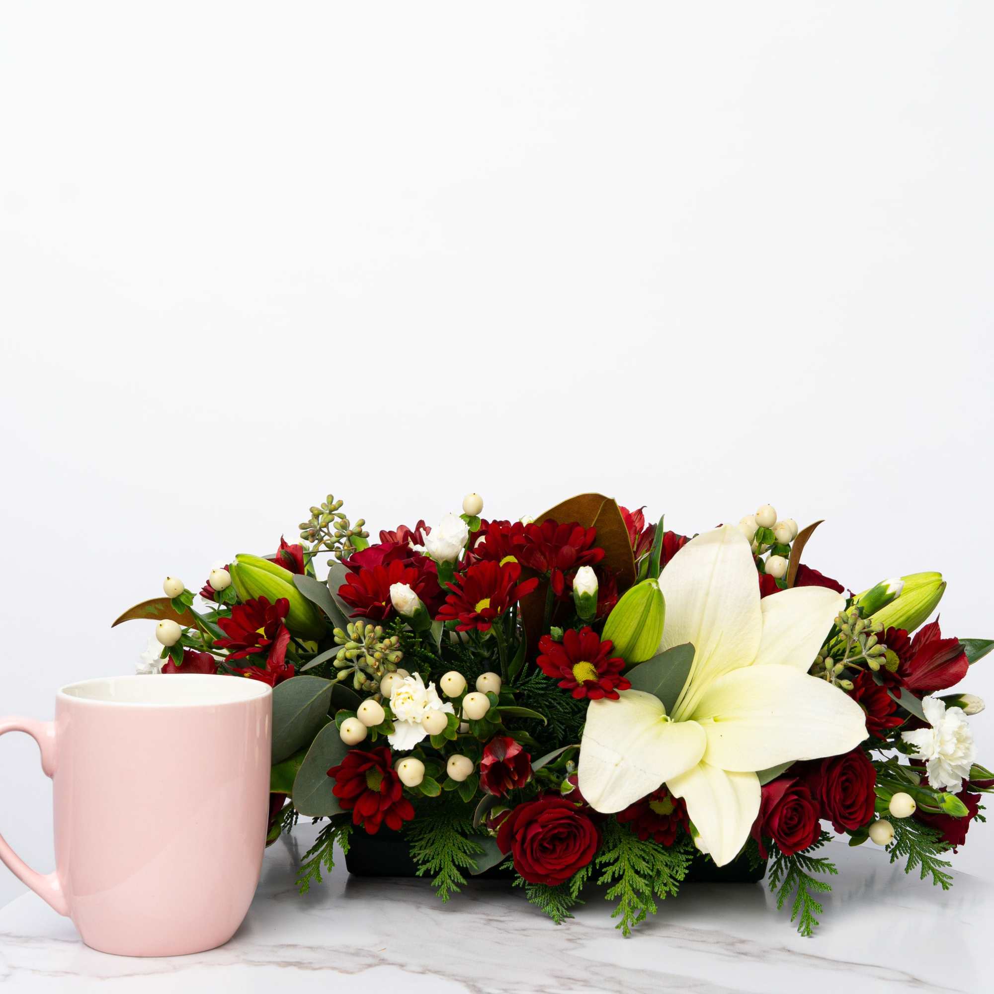 Red and white floral arrangement with a pink mug