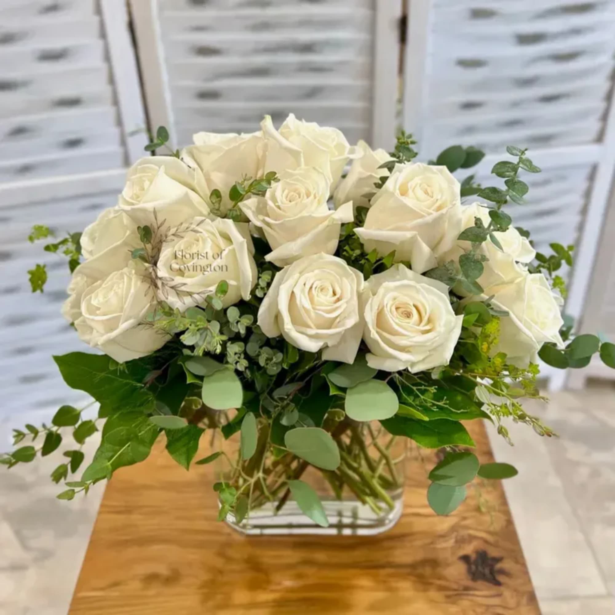 White roses arranged in a low glass vase with greenery