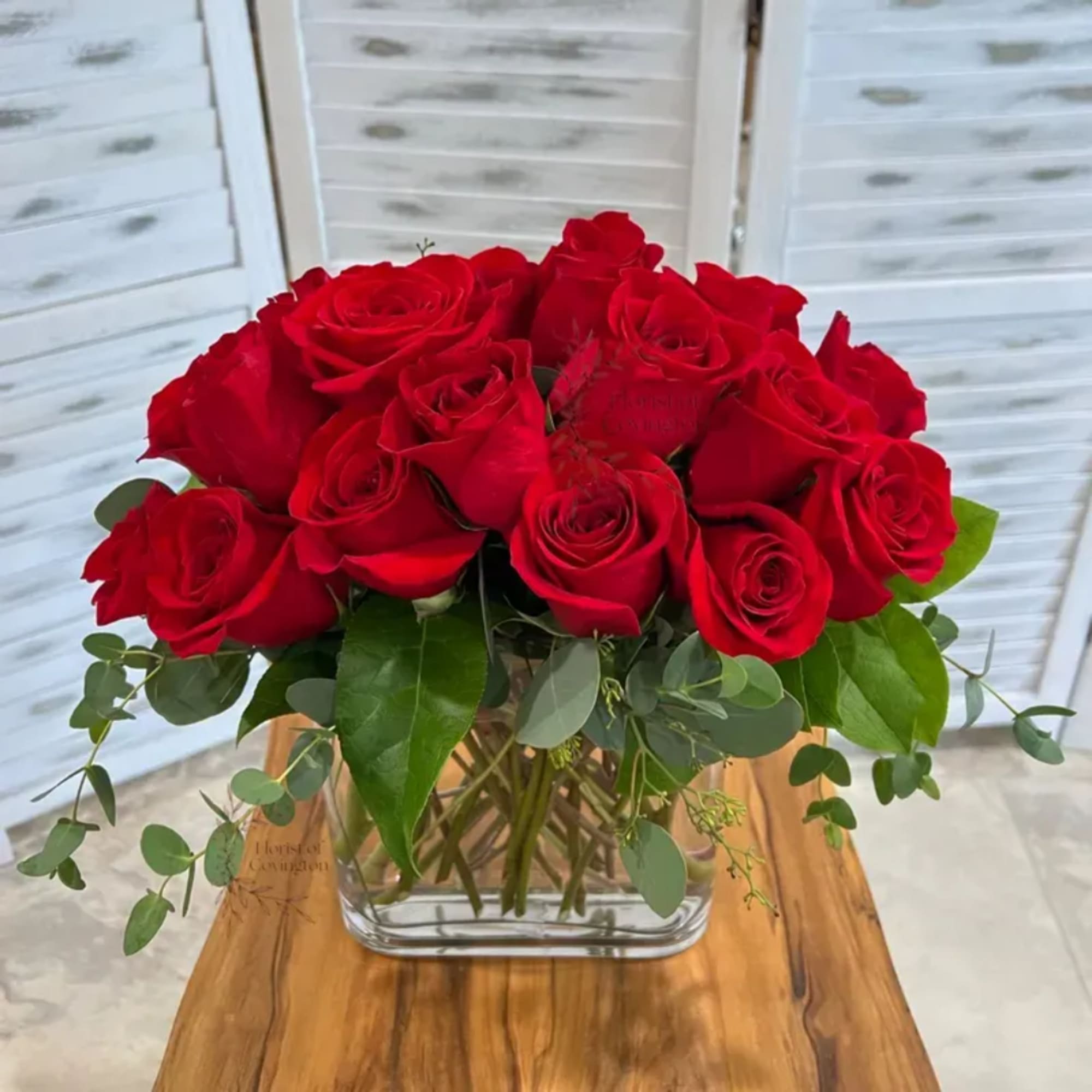 Red roses arranged in a clear glass vase with greenery
