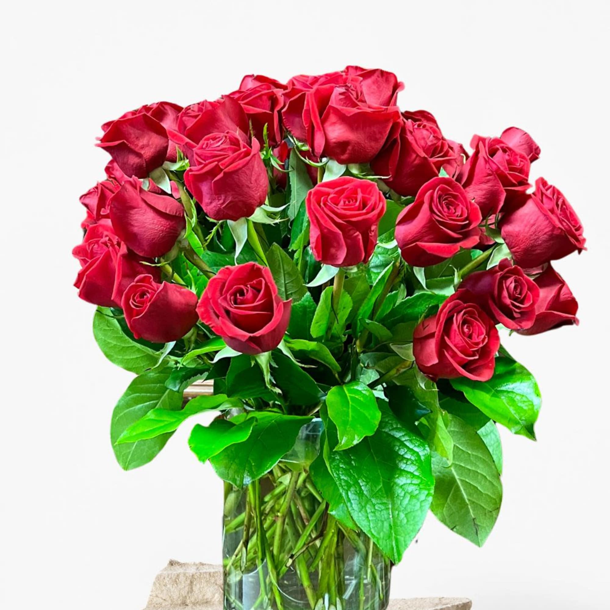 Arrangement of long-stem red roses in a clear glass vase with abundant foliage