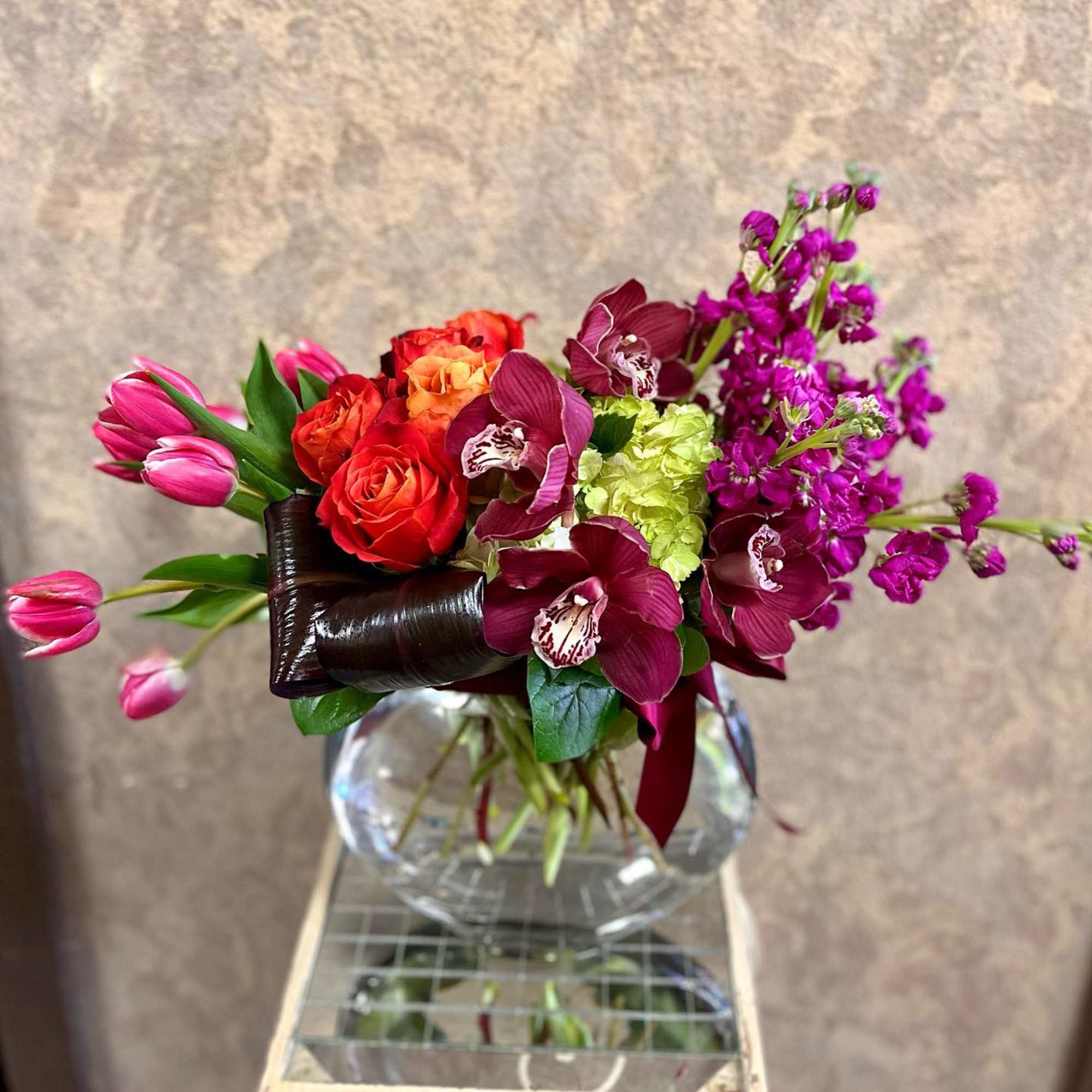 Bouquet of pink tulips, red roses, and purple orchids in a glass vase