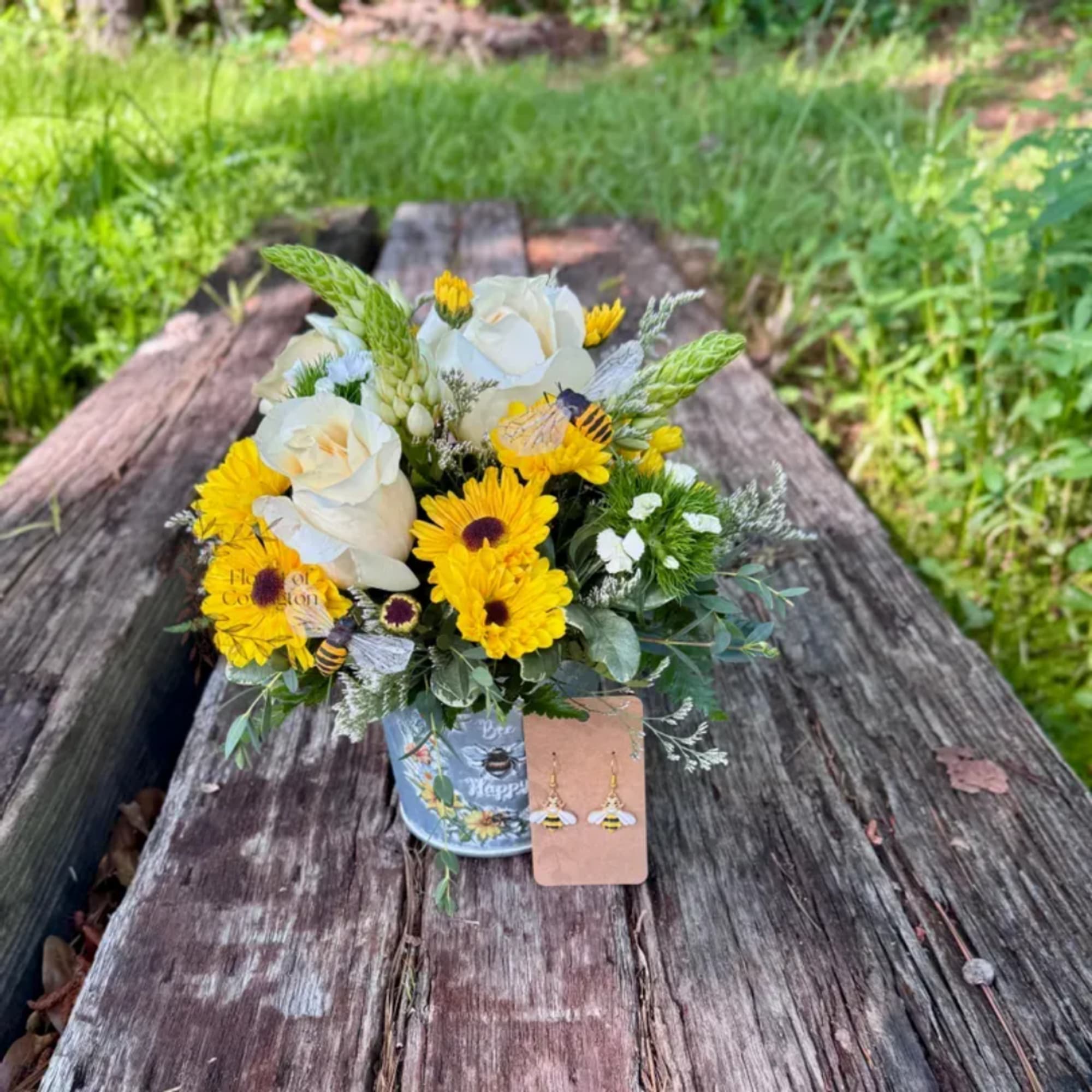 Yellow and white flower arrangement in a decorated tin container on a wooden bench