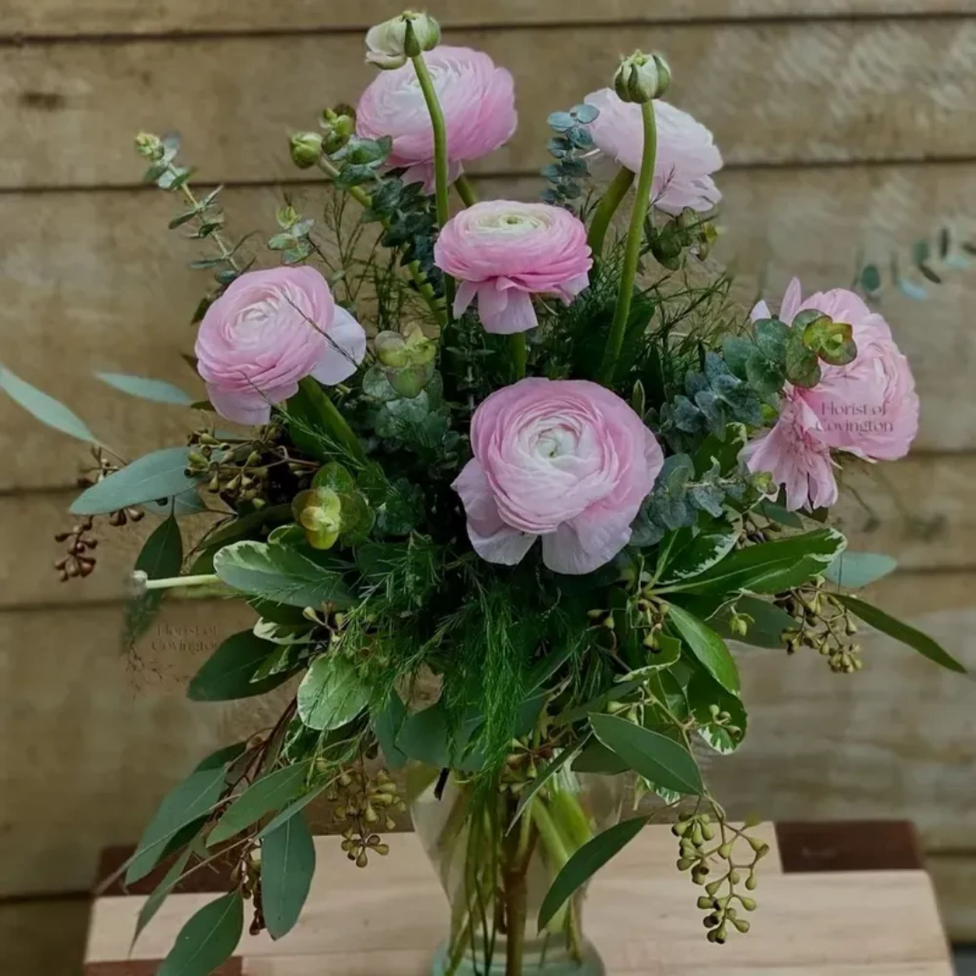Pink ranunculus bouquet in a clear glass vase with mixed greenery