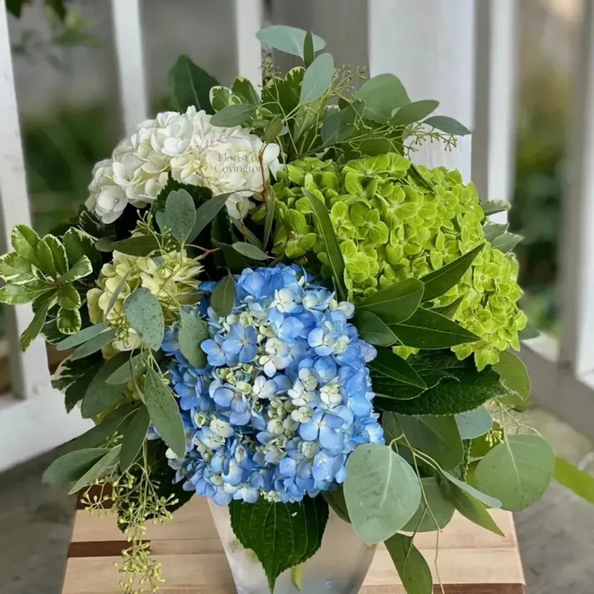 Blue, green, and white hydrangeas arranged in a vase with mixed foliage