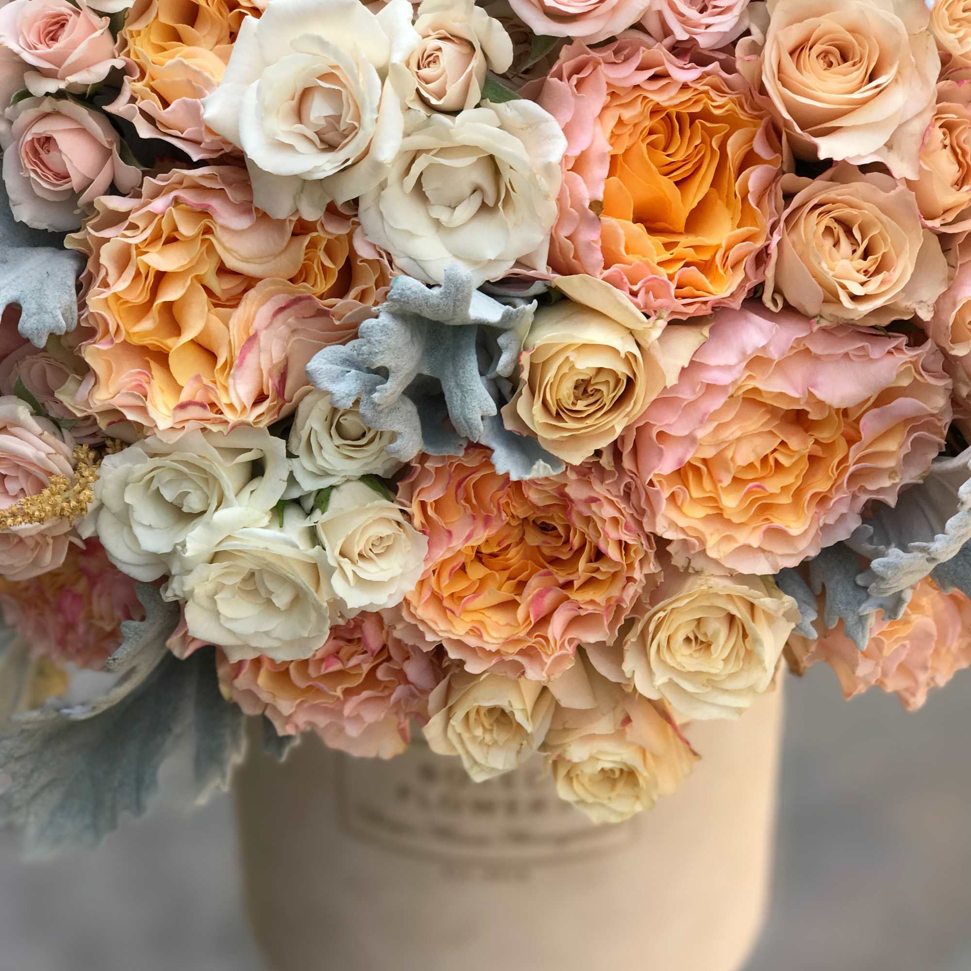Bouquet of peach, pink, and white roses in a cream vase