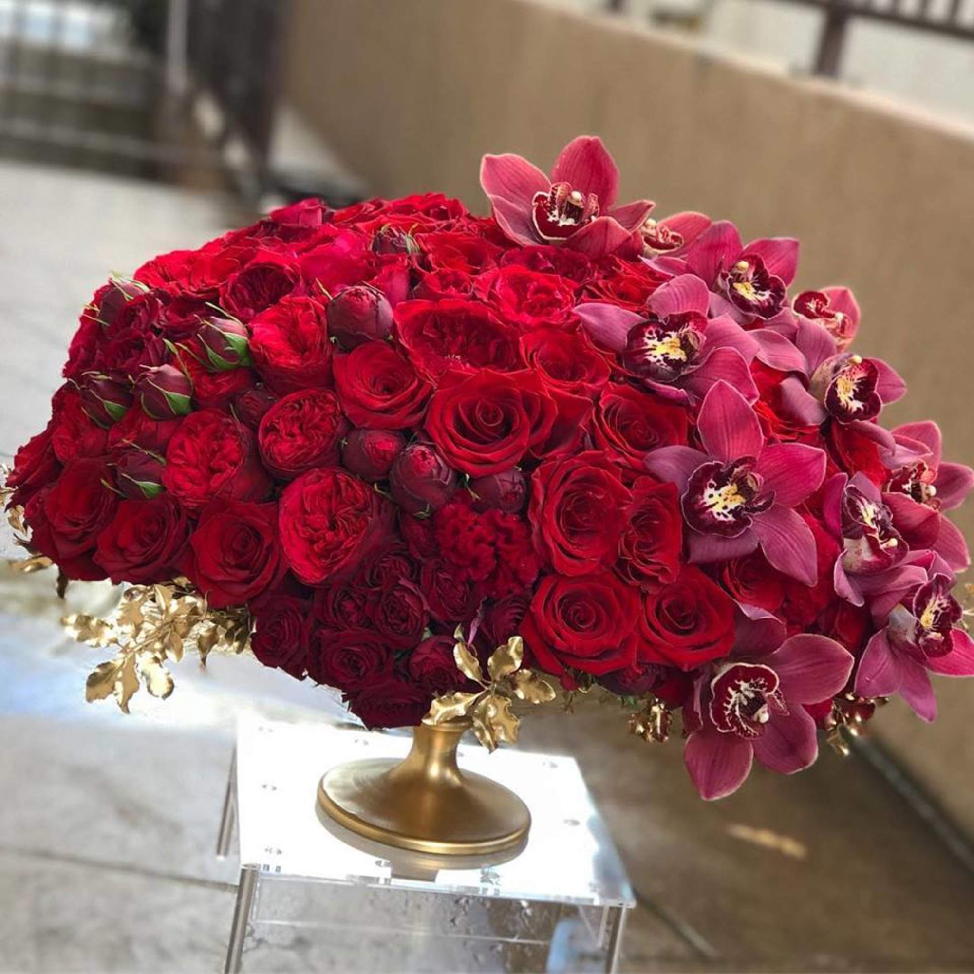 Large red rose arrangement with pink orchids in a gold pedestal vase