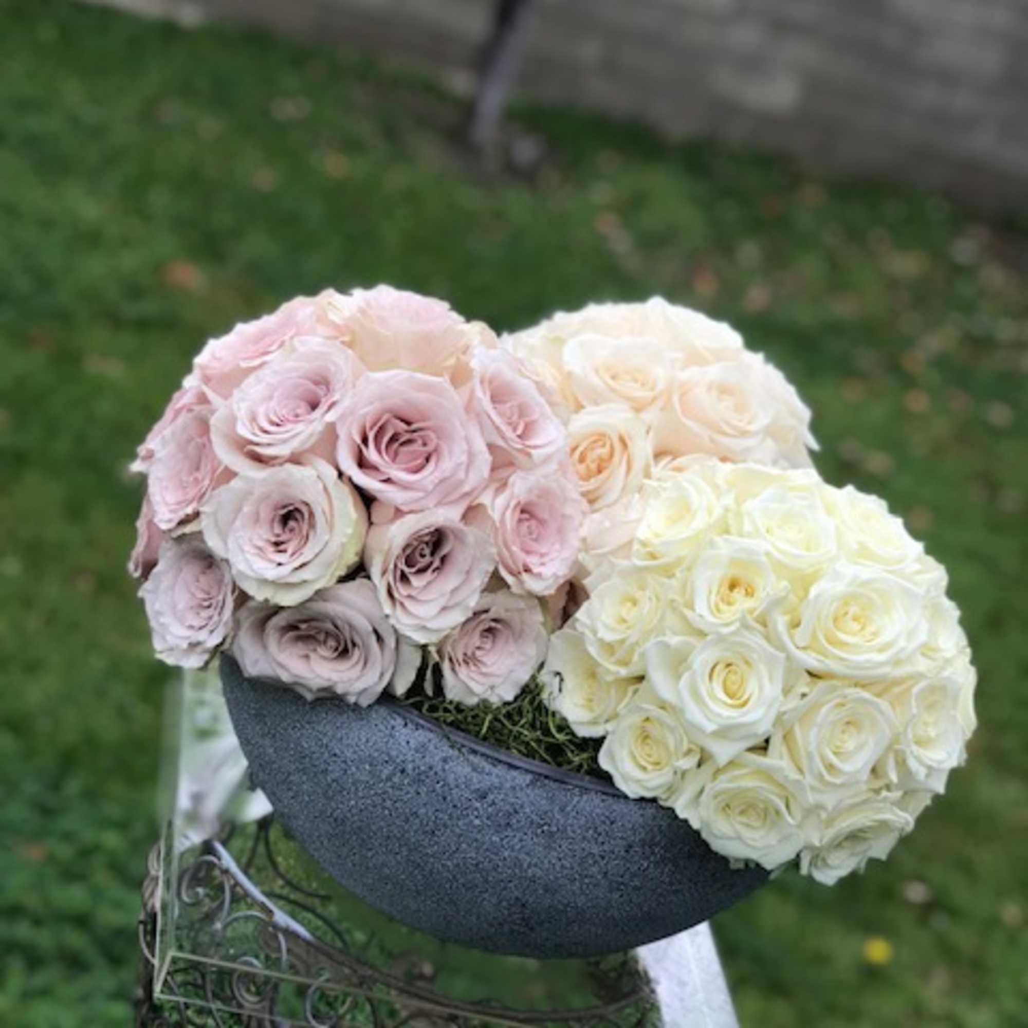 Two round bouquets of pale pink and cream roses in a dark container