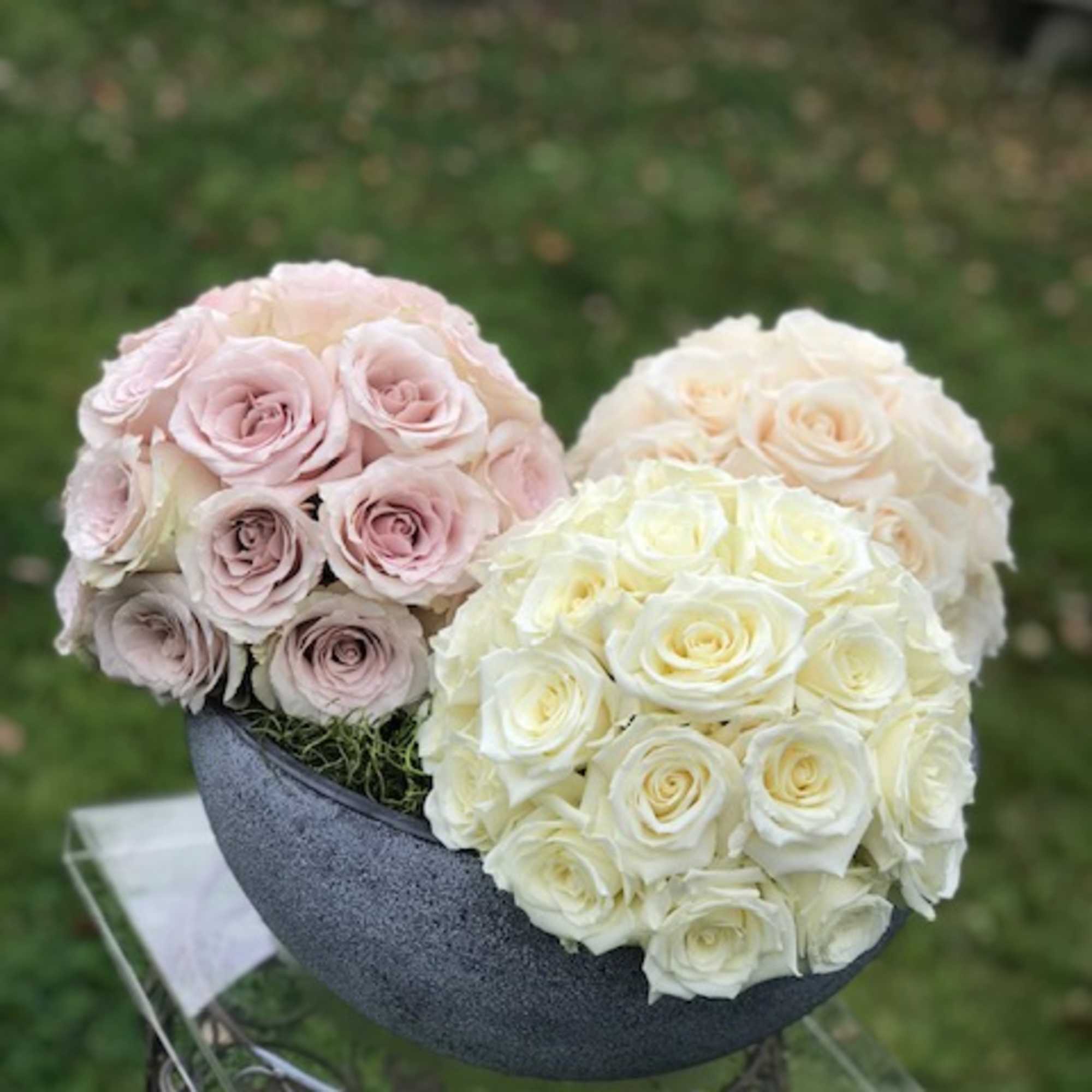 Three round rose bouquets in a gray bowl, in blush, cream, and white.