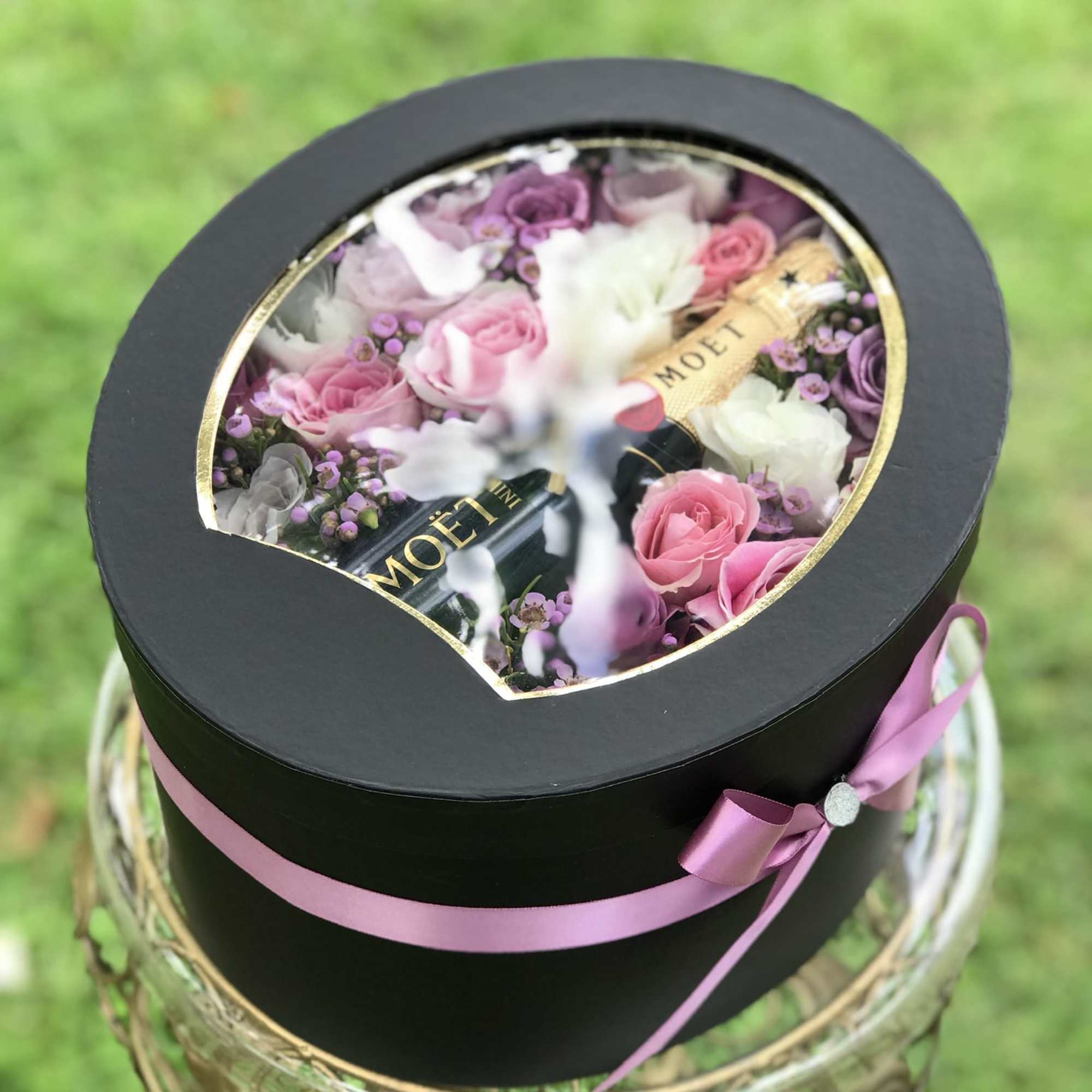 Round black gift box with pink and purple roses and champagne bottles