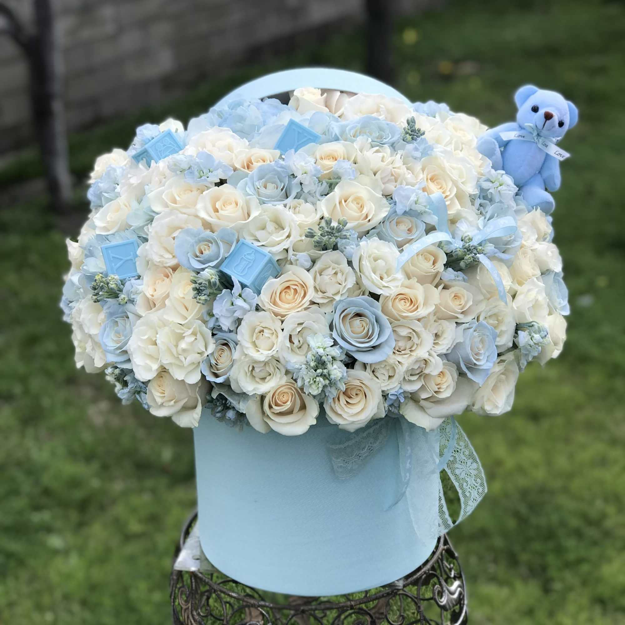Blue and white rose arrangement in a round hatbox with a teddy bear