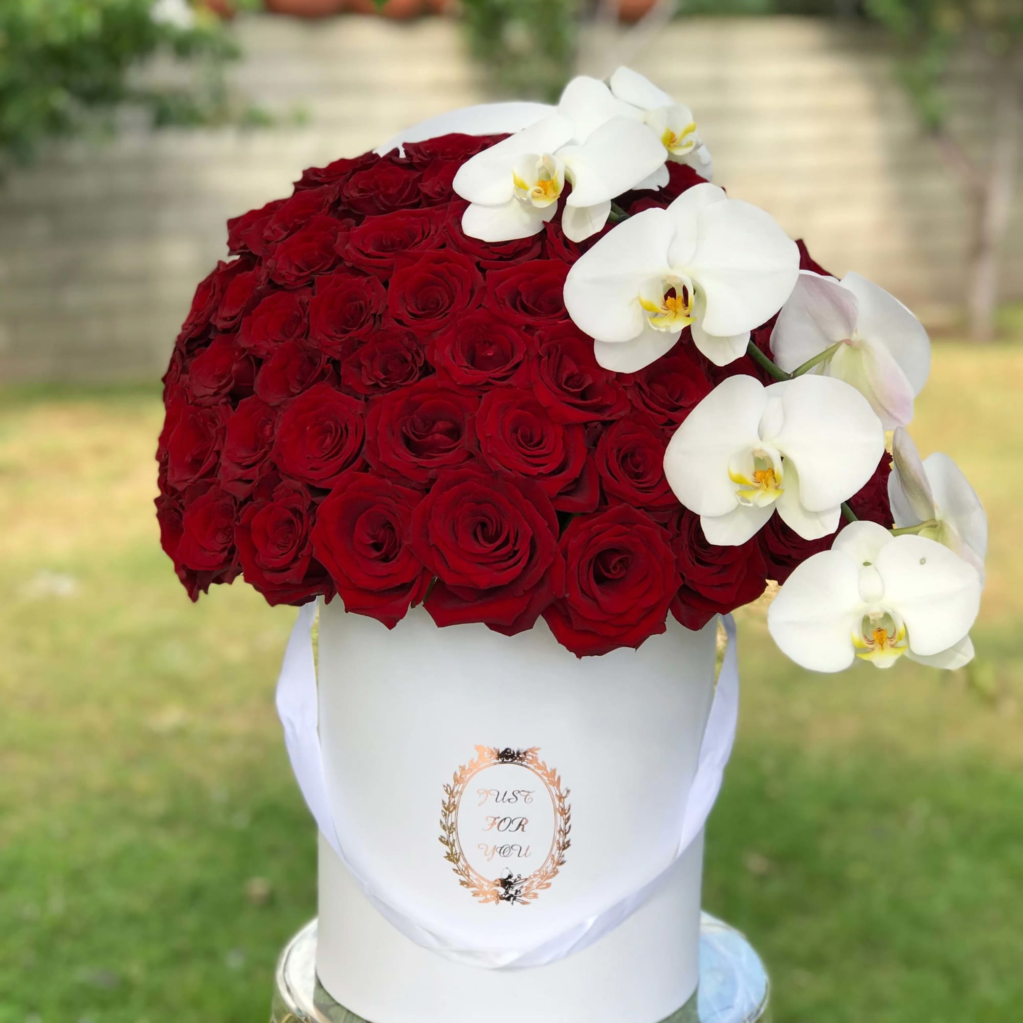 Red rose arrangement in a white hatbox with white orchids