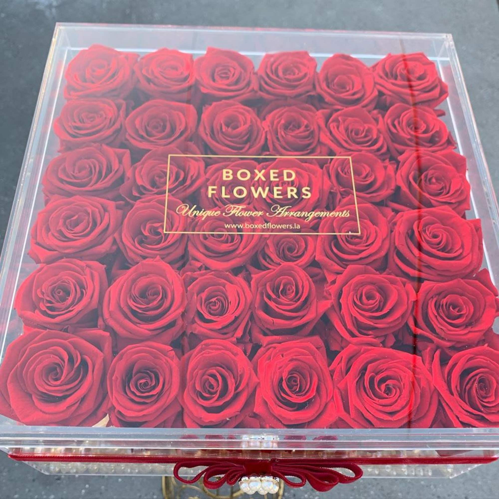 Box of red roses under a clear lid with a ribbon closure