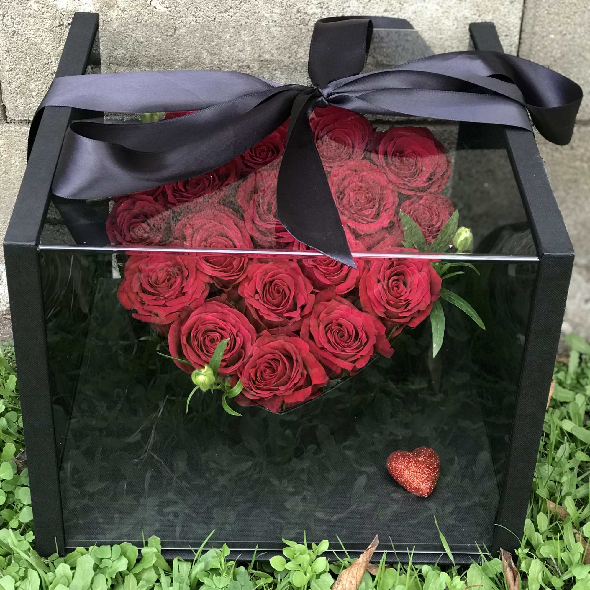 Heart-shaped red rose arrangement in a black gift box with a ribbon bow