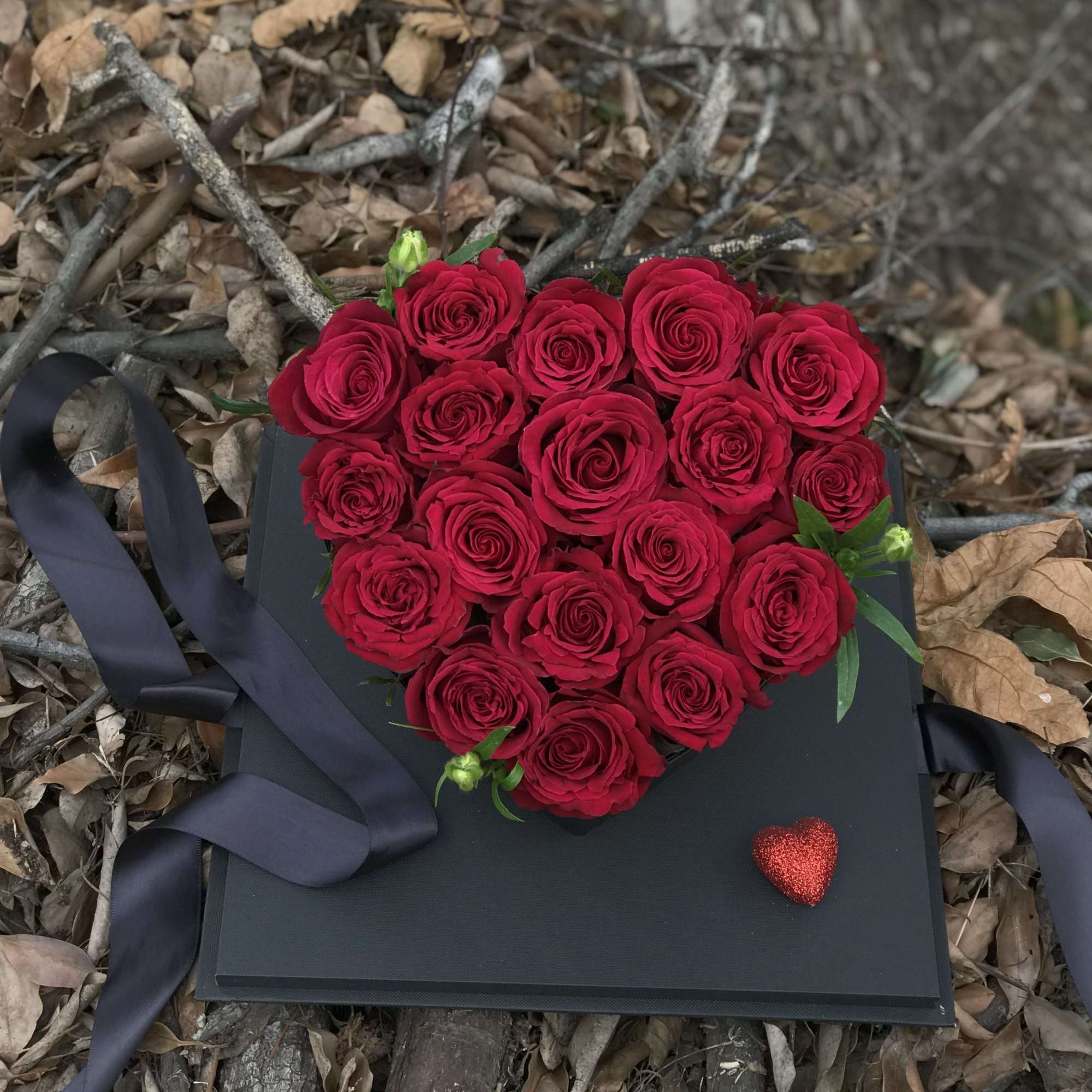 Heart-shaped bouquet of red roses on a black box with ribbon