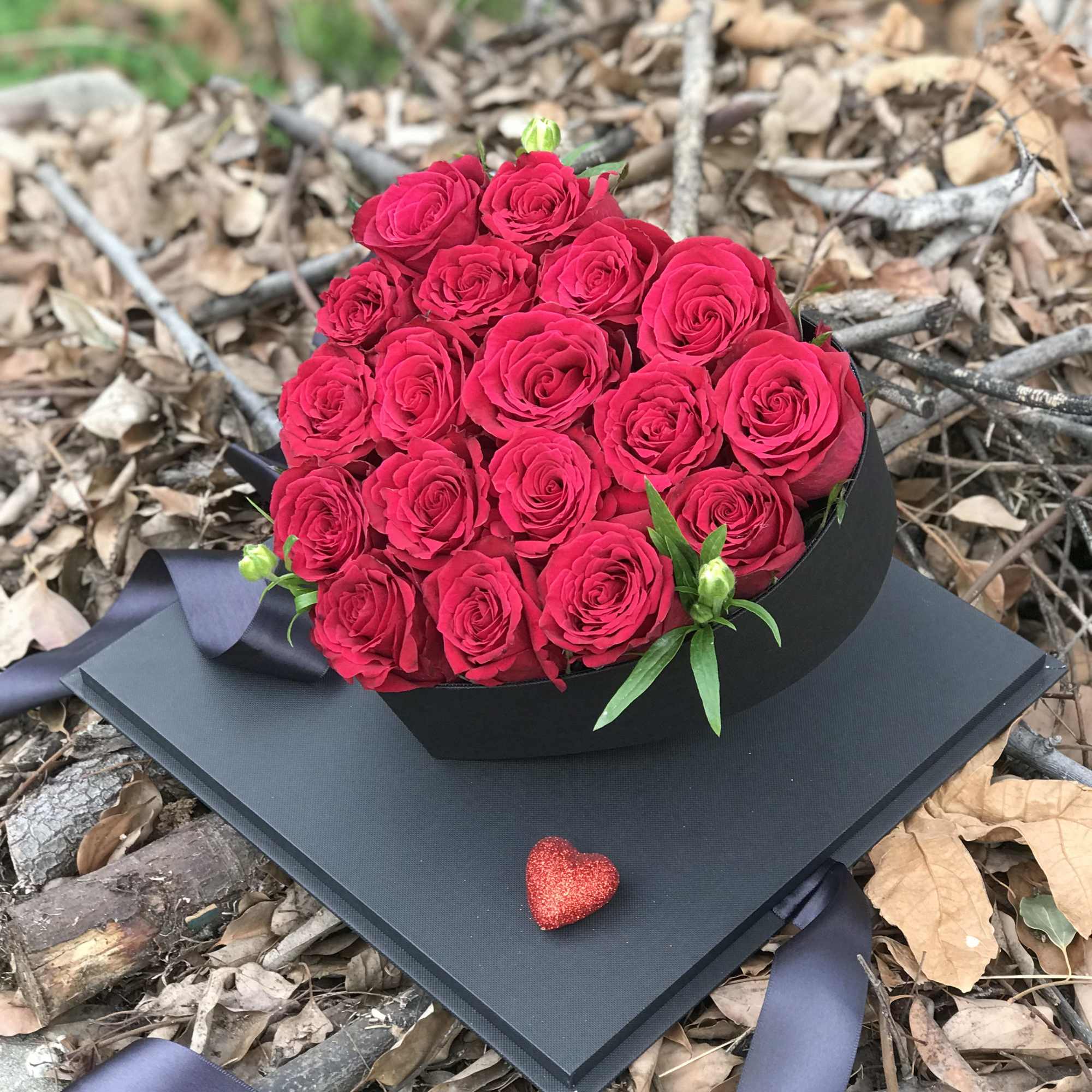 Heart-shaped bouquet of red roses in a black box with a small glitter heart