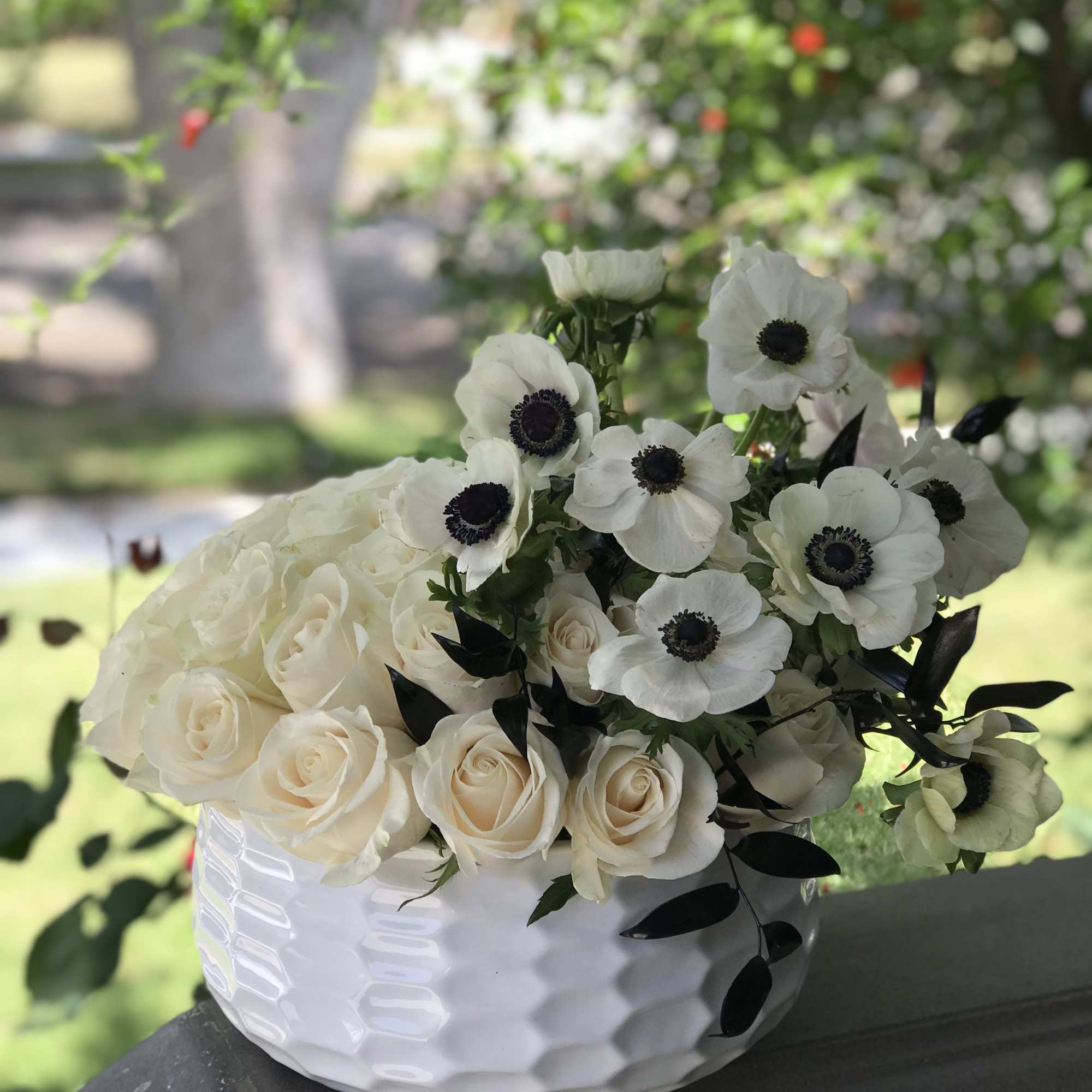 White roses and anemones arranged in a white bowl vase