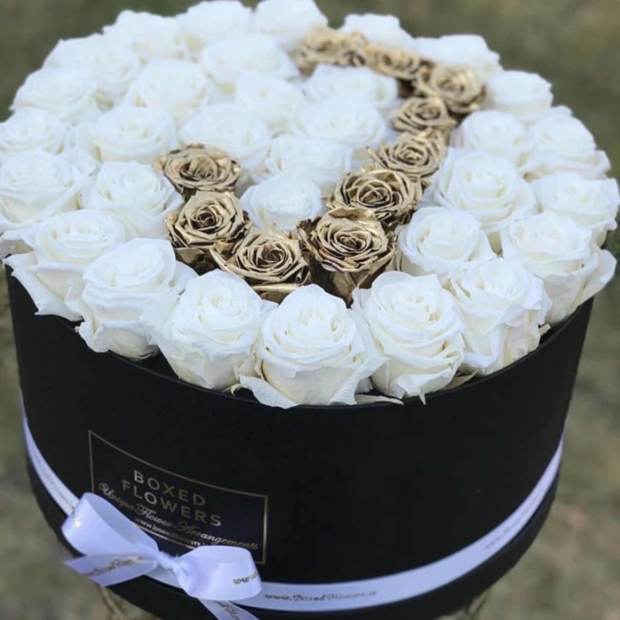 White roses and gold roses arranged in a black round box