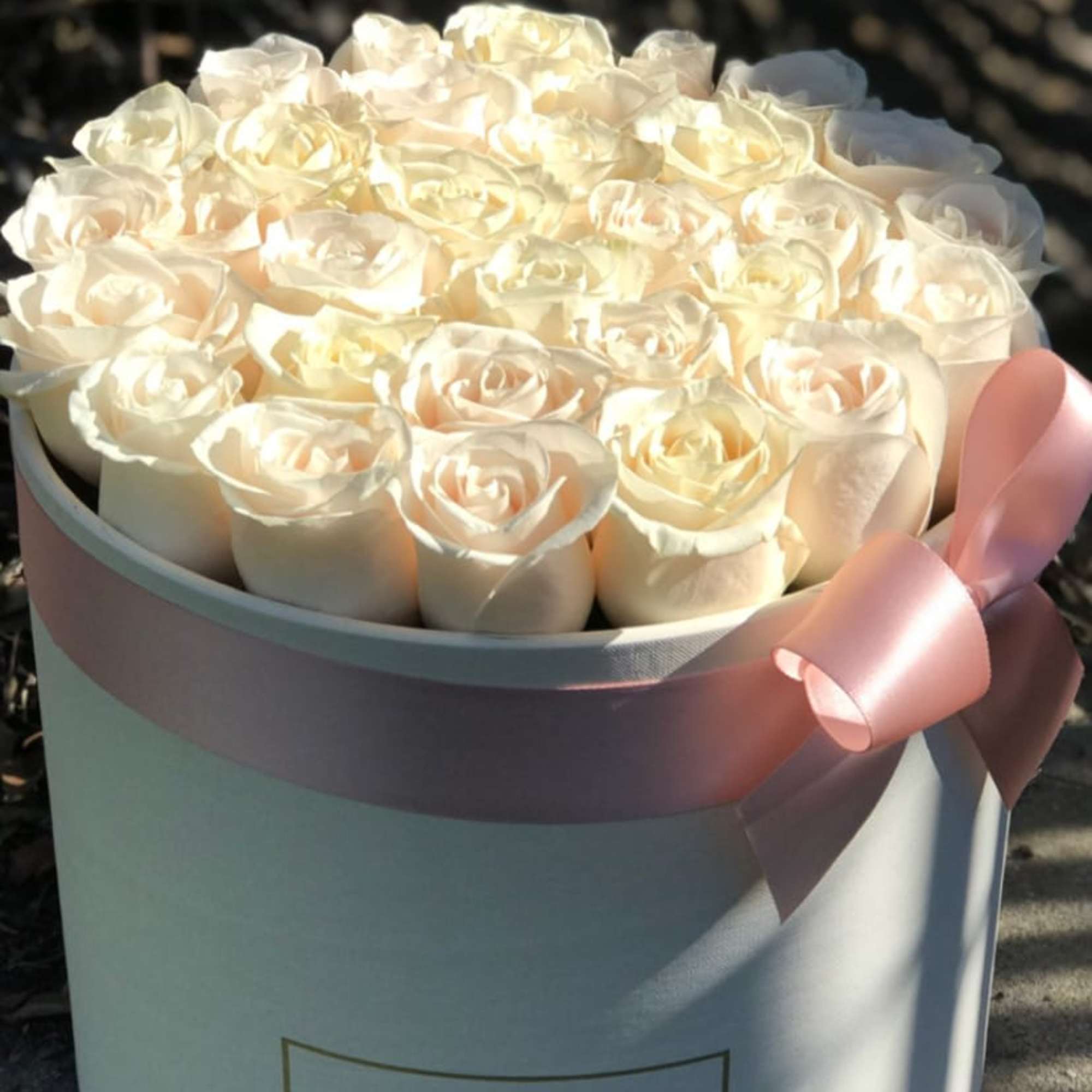 White roses arranged in a round hat box with a pink ribbon.