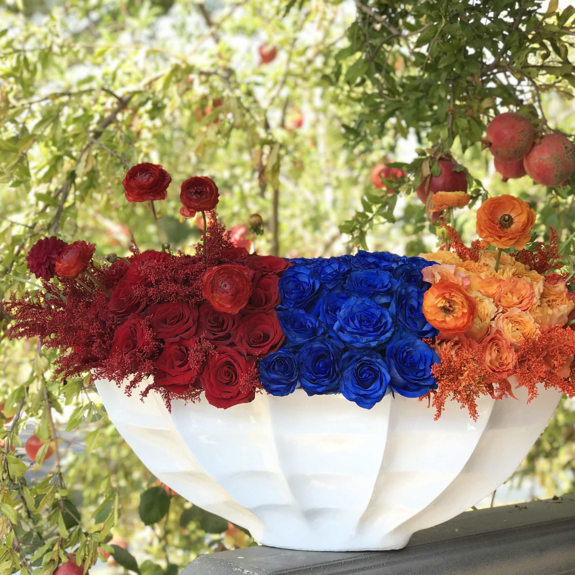 Large bowl arrangement of red, blue, and orange roses in a white vase