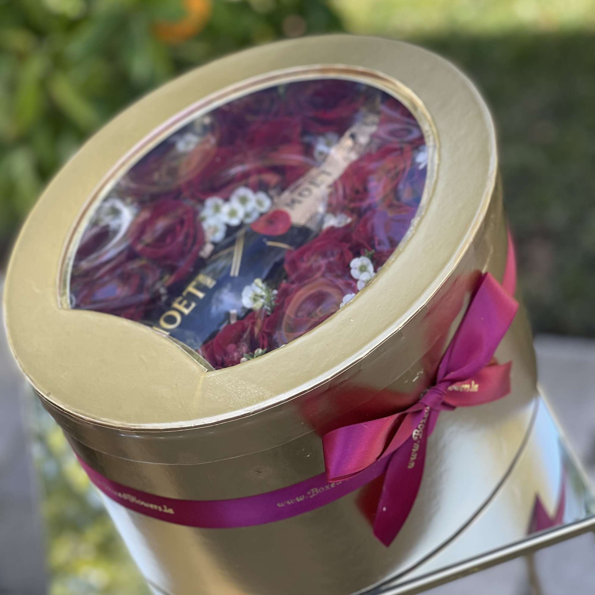 Round gold gift box with red roses and a champagne bottle inside
