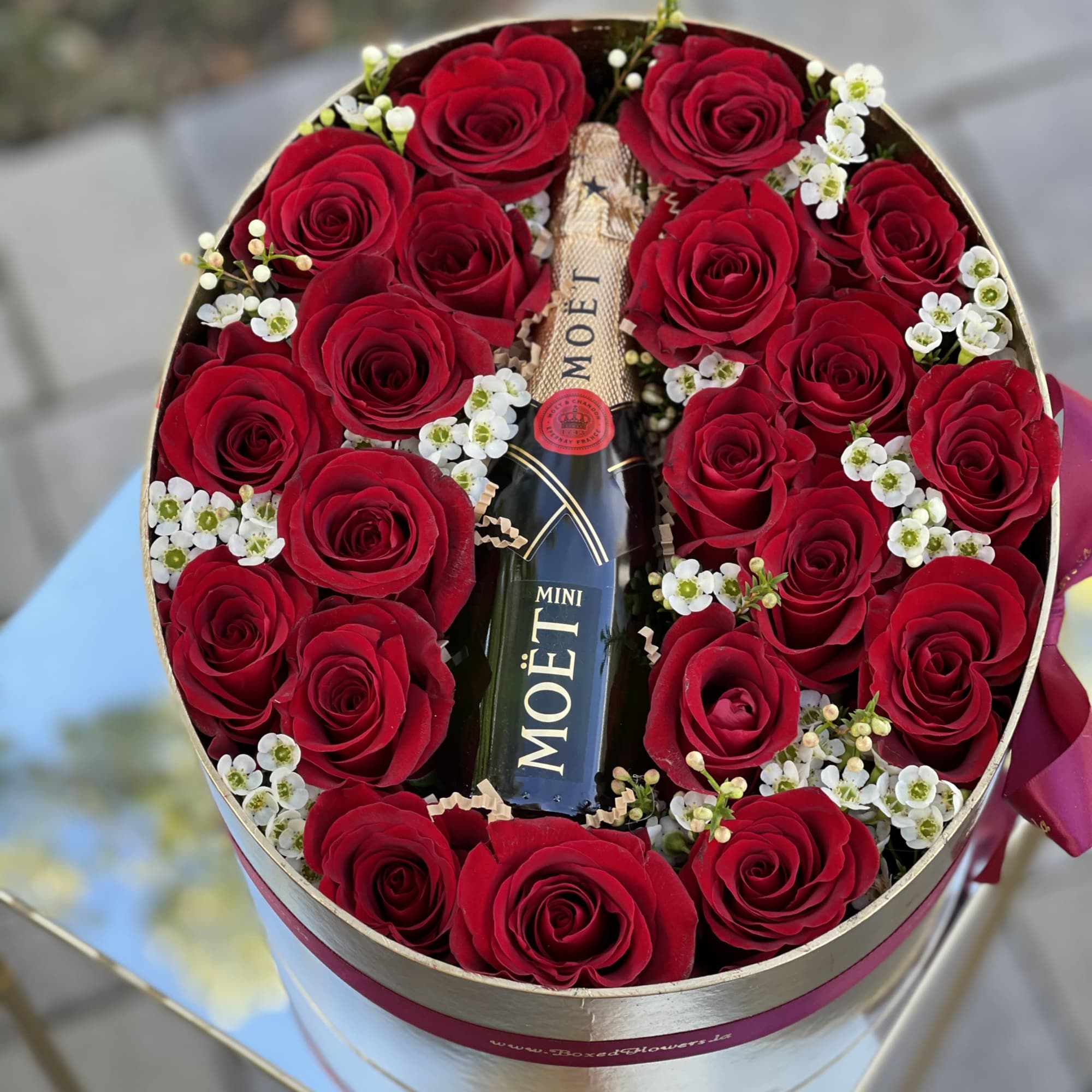 Red roses arranged around a Moët champagne bottle in a round box