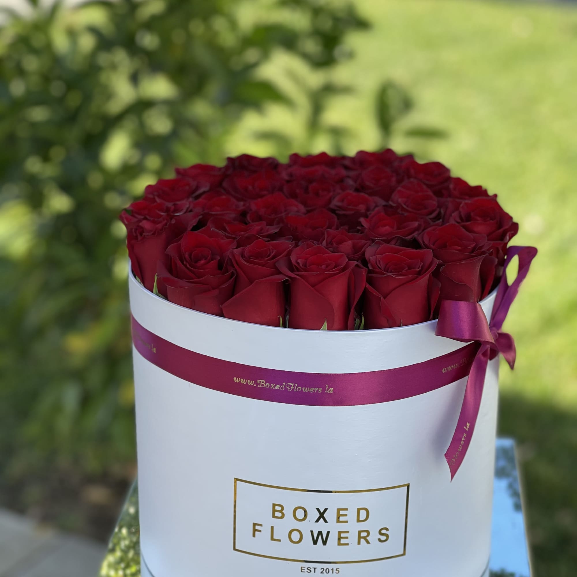 Red roses arranged in a white round box with a purple ribbon