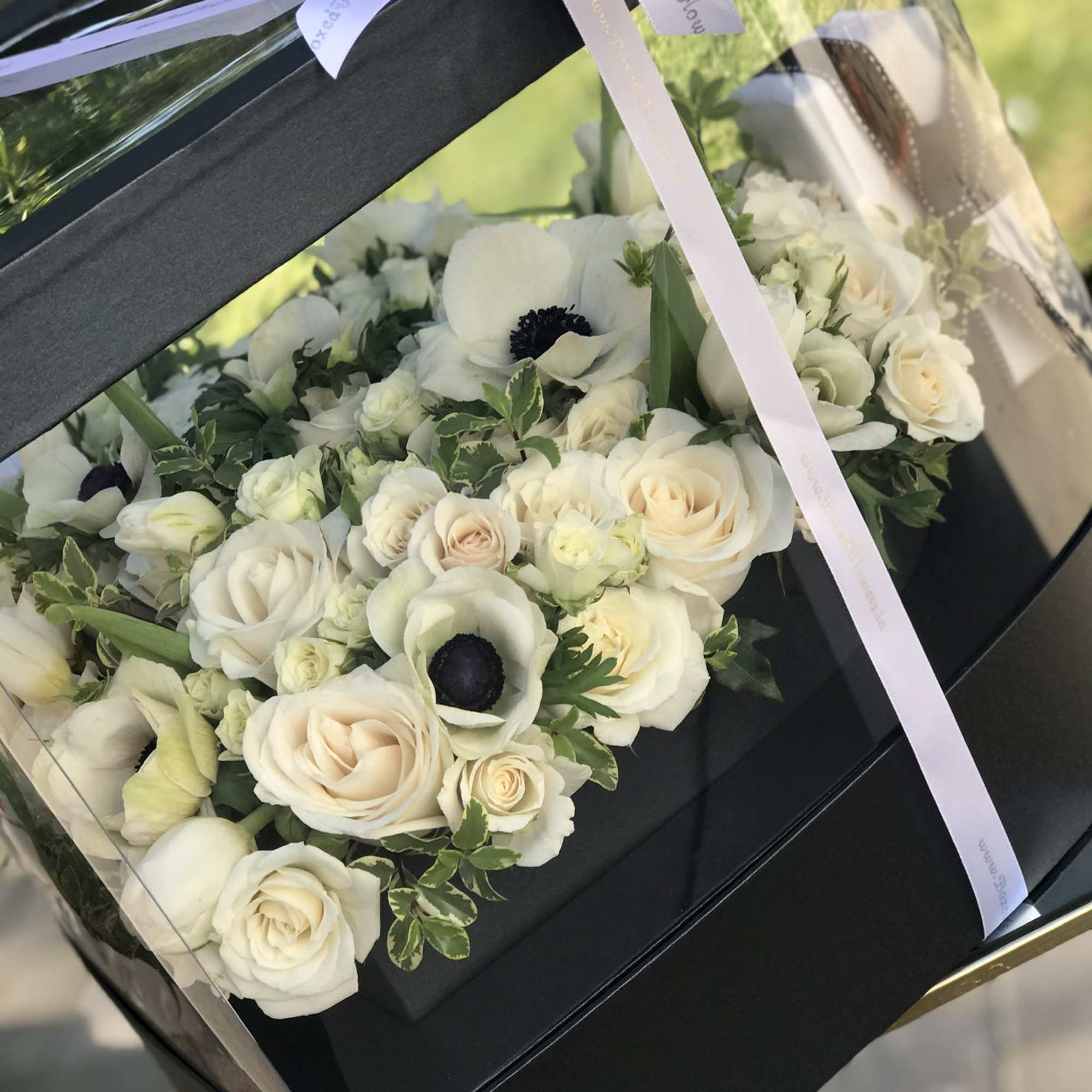 White roses and anemones in a black gift box with a ribbon