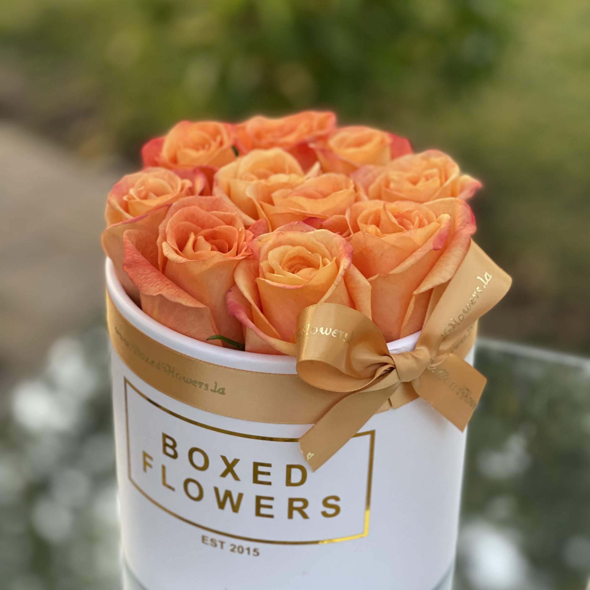 Orange roses arranged in a white hat box with a gold ribbon