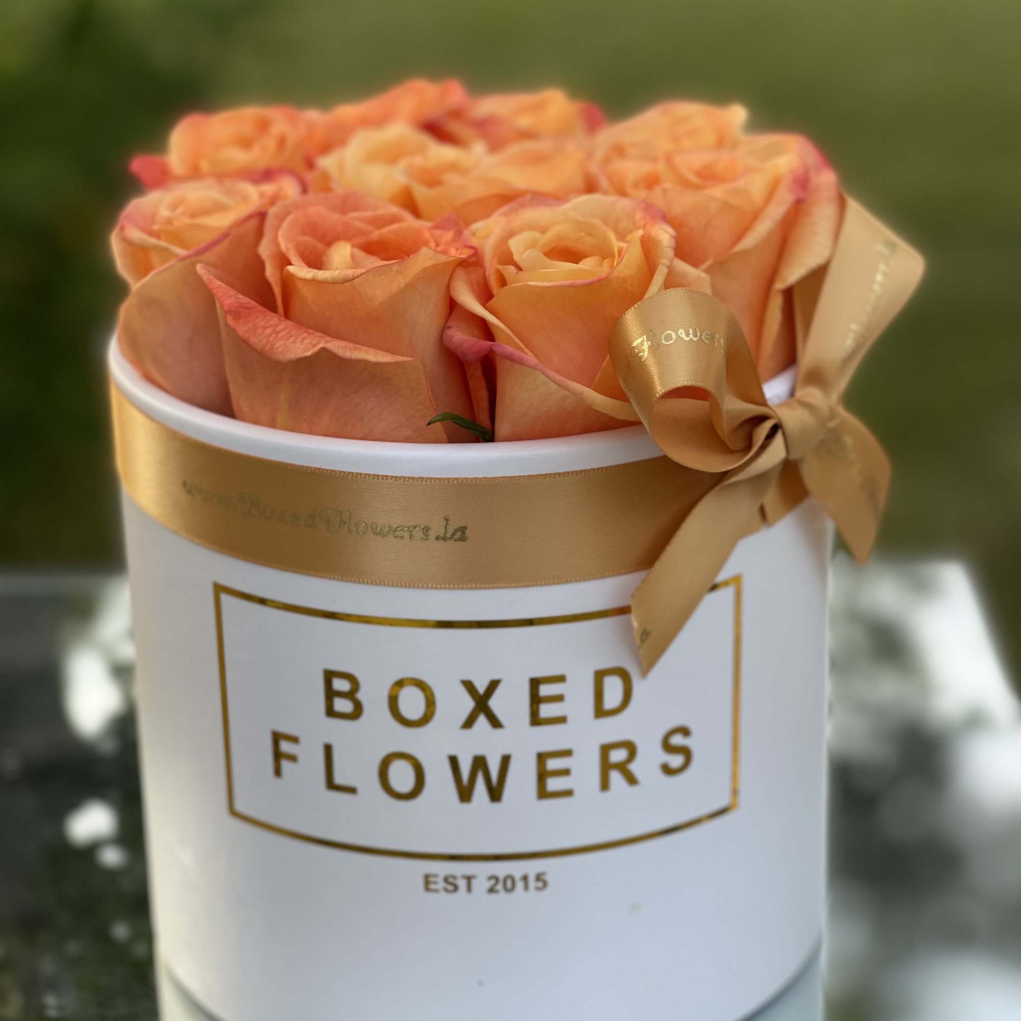 Peach roses arranged in a white hat box with a gold ribbon
