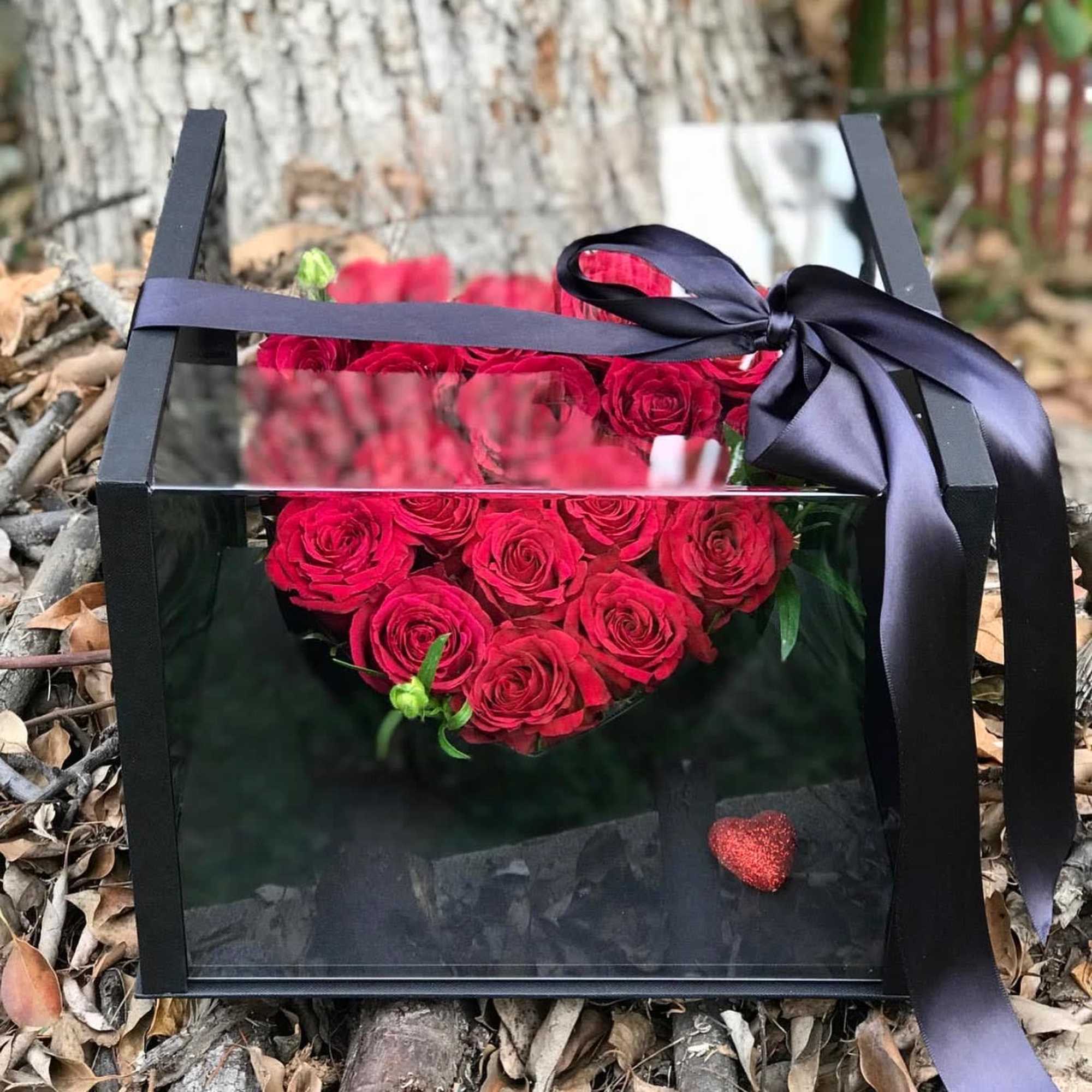 Red roses arranged in a black gift box with a ribbon bow
