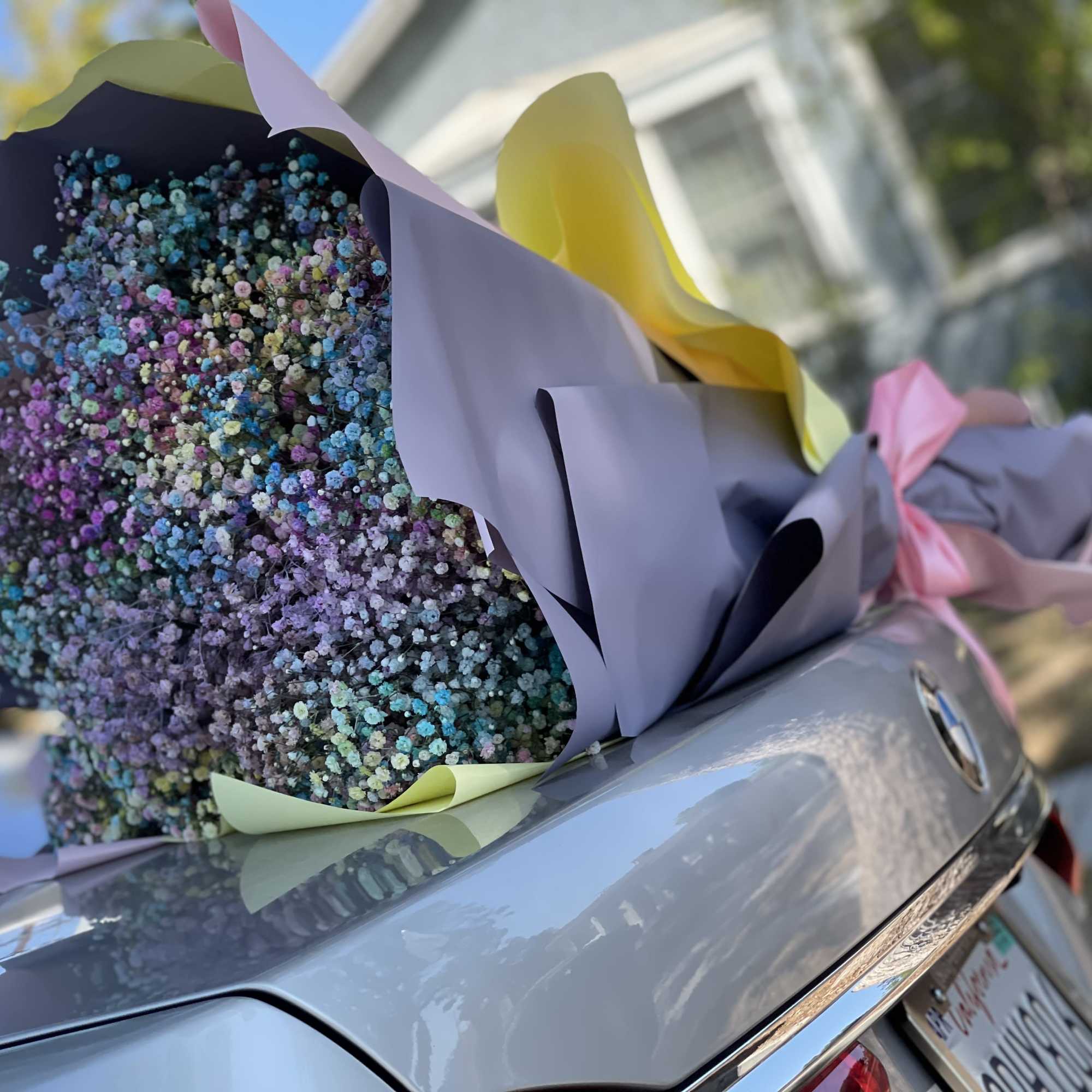 Large bouquet of tiny multicolored flowers wrapped in pastel paper on a car trunk