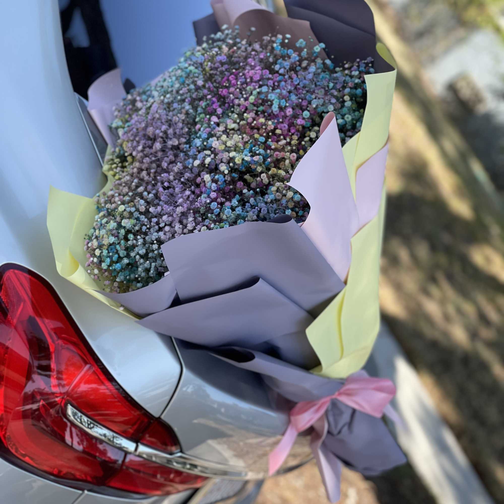 Pastel-wrapped bouquet of tiny multicolored flowers resting on a car trunk