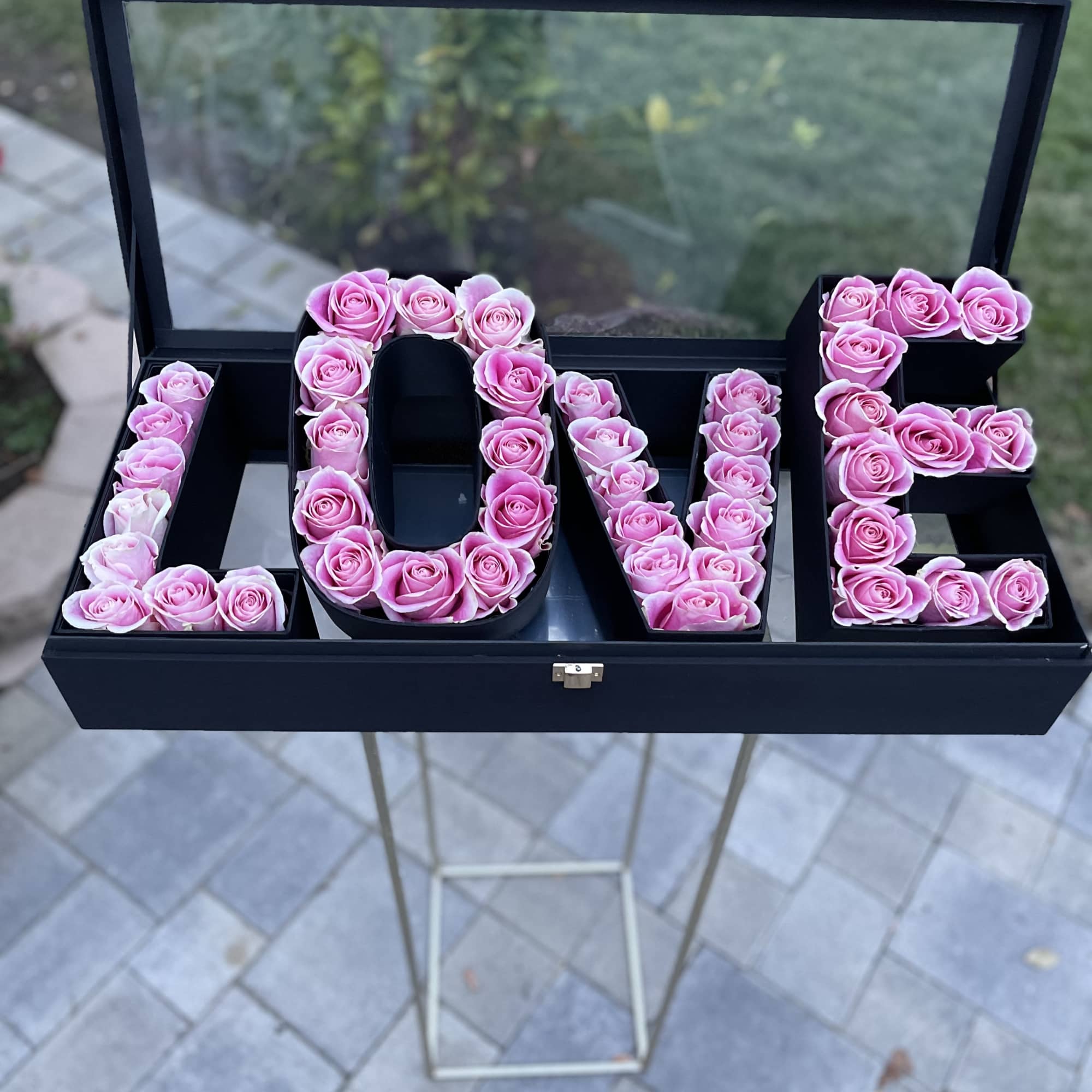 Pink roses arranged to spell LOVE in a black display box