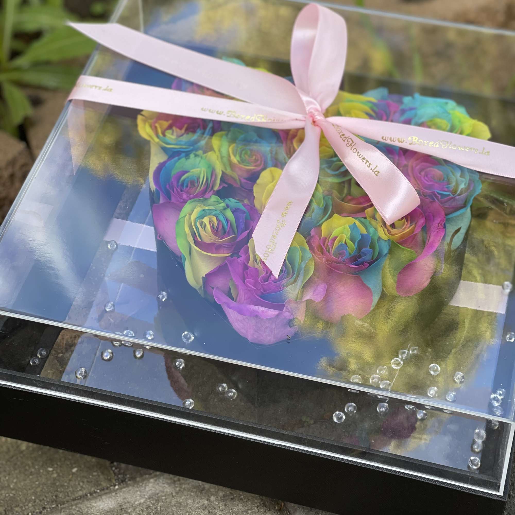 Rainbow-colored roses in a clear gift box tied with a pink ribbon